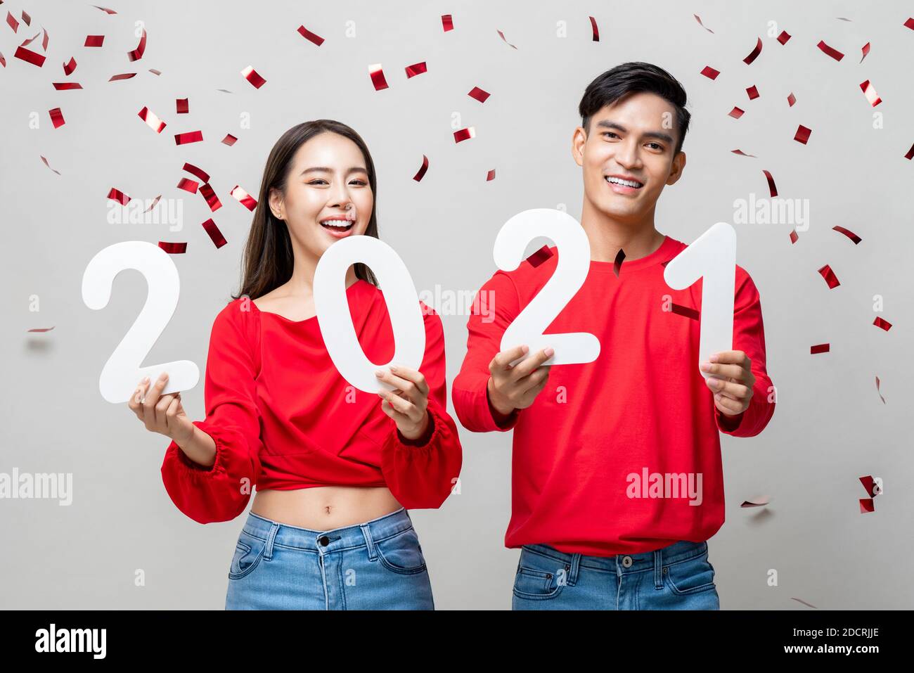 Portrait d'un couple asiatique souriant en tenue décontractée rouge 2021 numéros pour le nouveau concept de l'année en gris clair arrière-plan avec confetti Banque D'Images