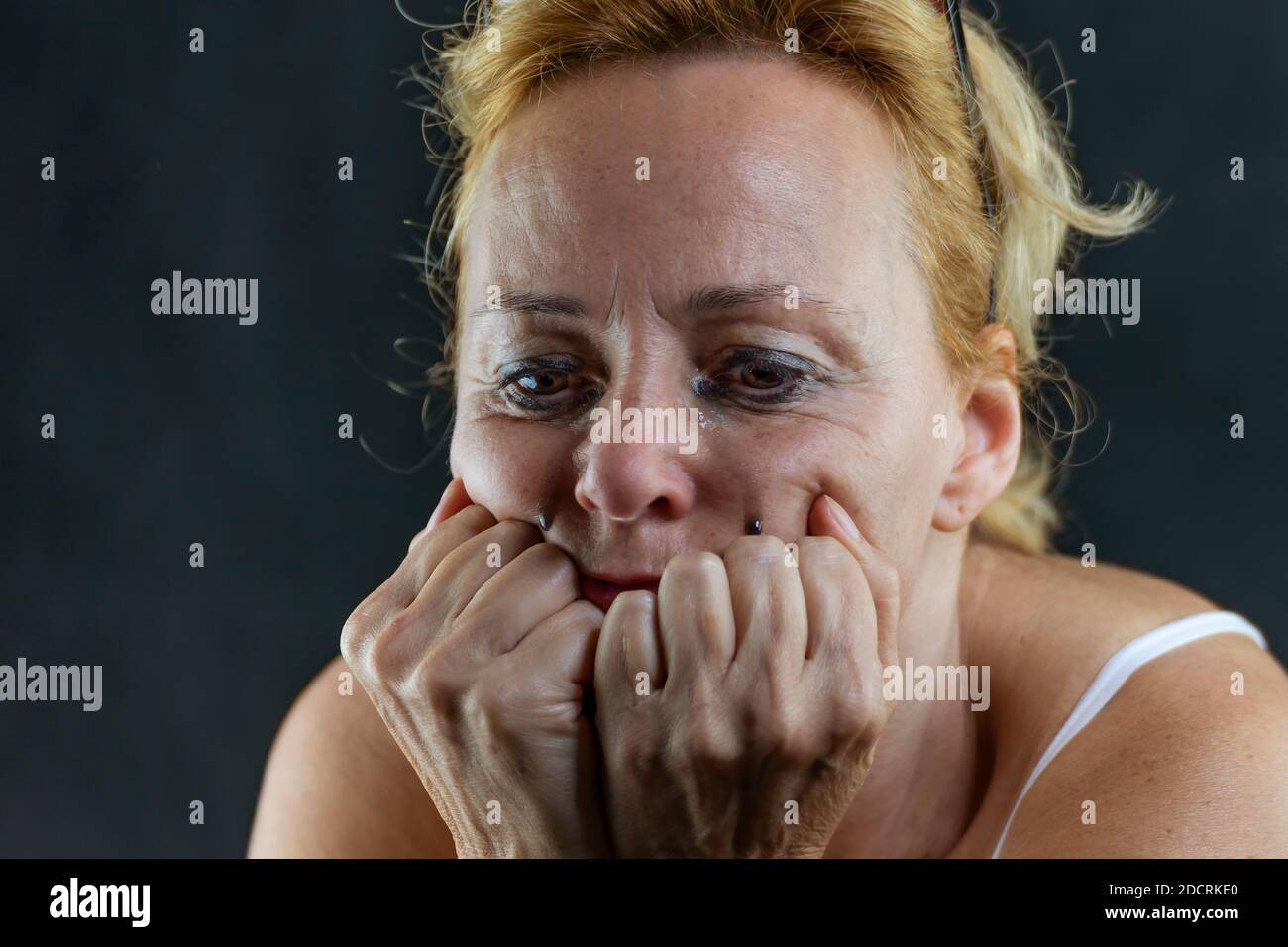 Une femme blanche d'âge moyen pleure avec son visage reposant ses mains et a le maquillage goutte de ses yeux Banque D'Images