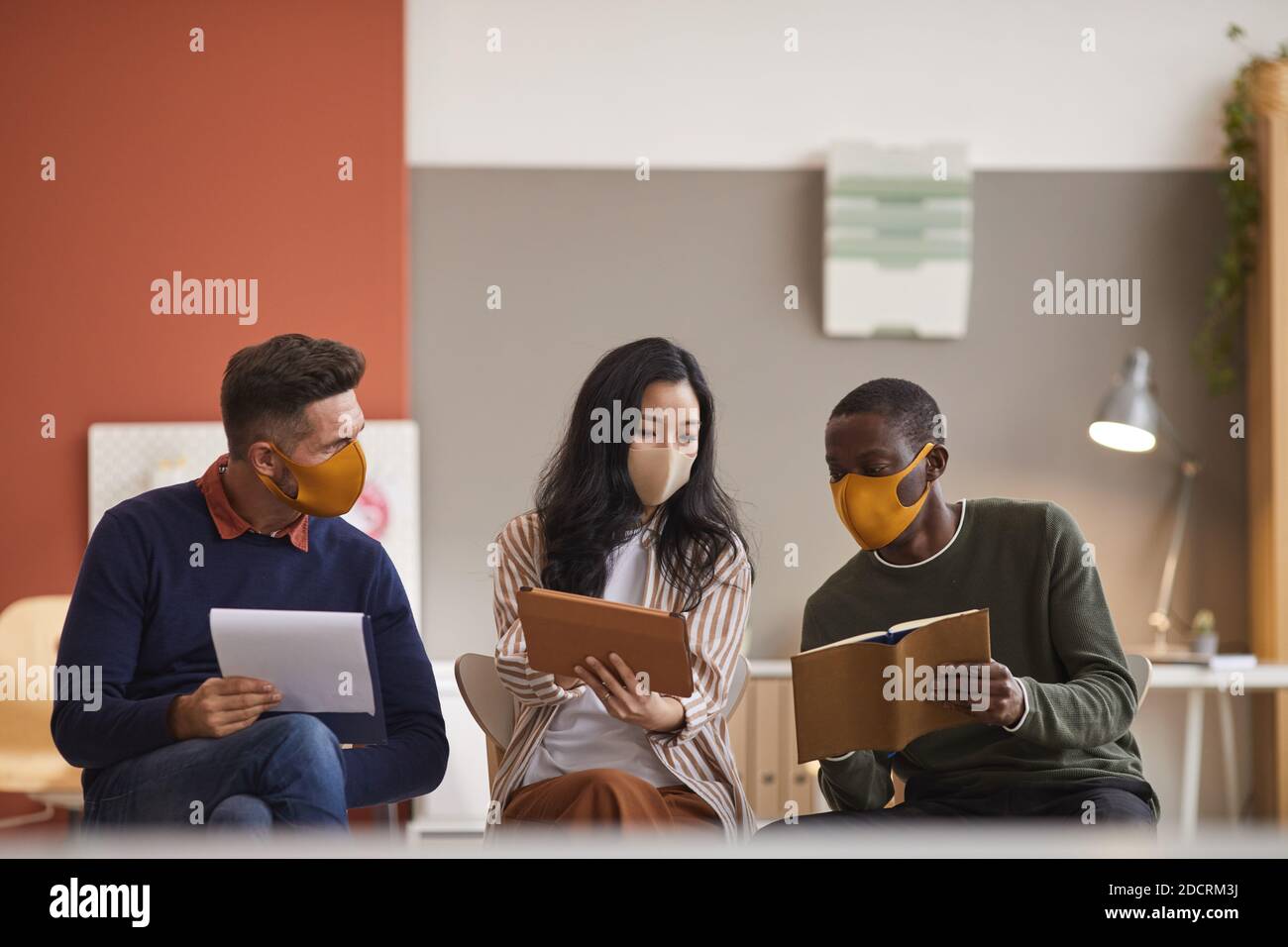 Groupe multiethnique de trois hommes d'affaires portant des masques de visage pendant discuter du projet au bureau Banque D'Images