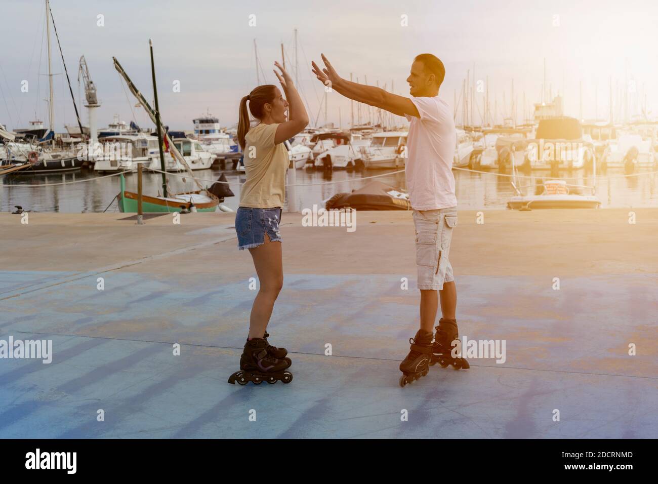 Jeune beau couple de patinage à roulettes donnant cinq mains hautes au coucher du soleil dans le parc de skate à côté du port en été.Friendship style de vie concept, succ Banque D'Images