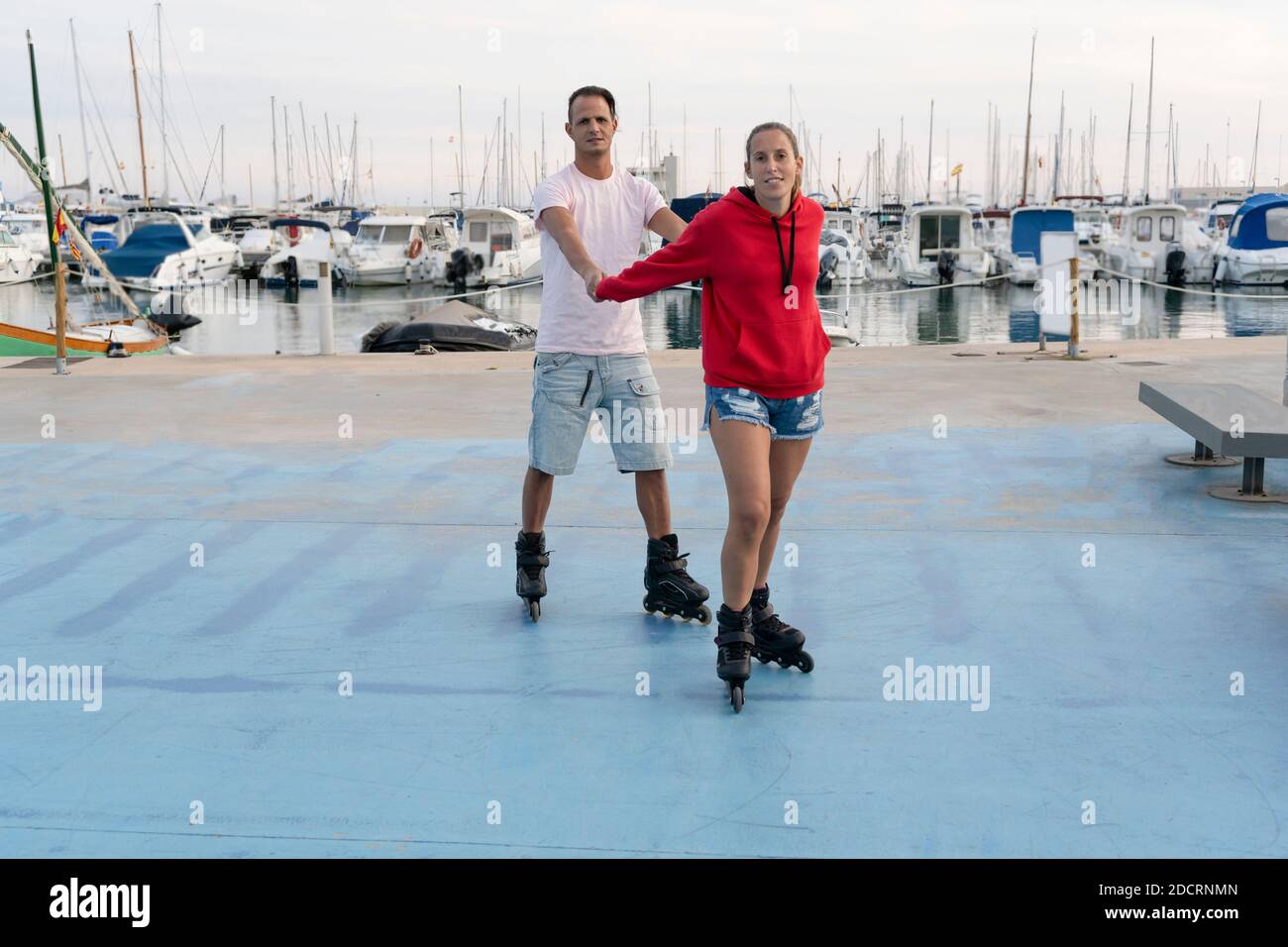 Jeune couple heureux patinage à roulettes dans le parc de skate à côté du beau port en été.Friendship sport et concept de style de vie de forme physique. Banque D'Images