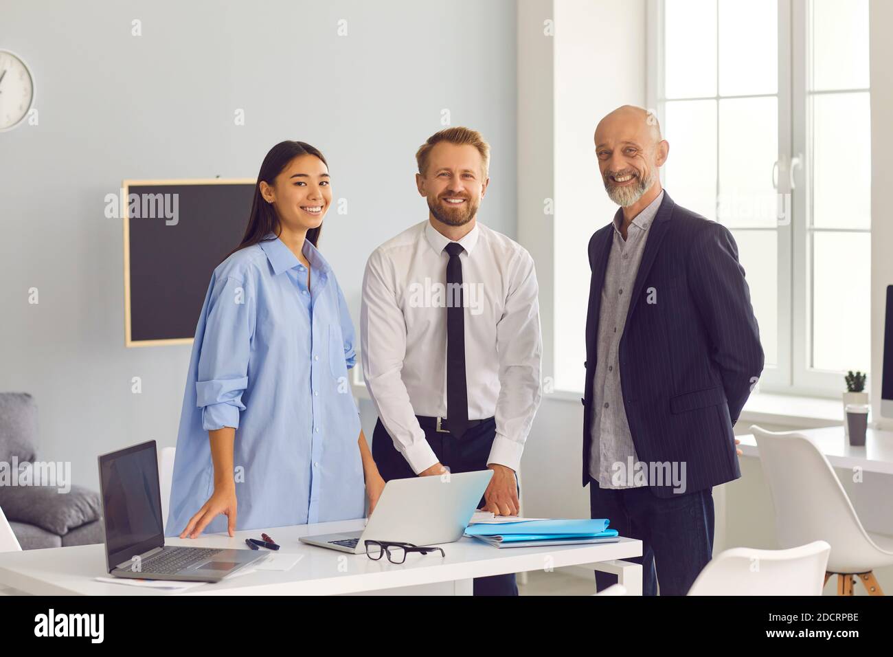 Une équipe diversifiée d'employés souriants de l'entreprise se tenant près du bureau ordinateurs portables qui regardent l'appareil photo Banque D'Images