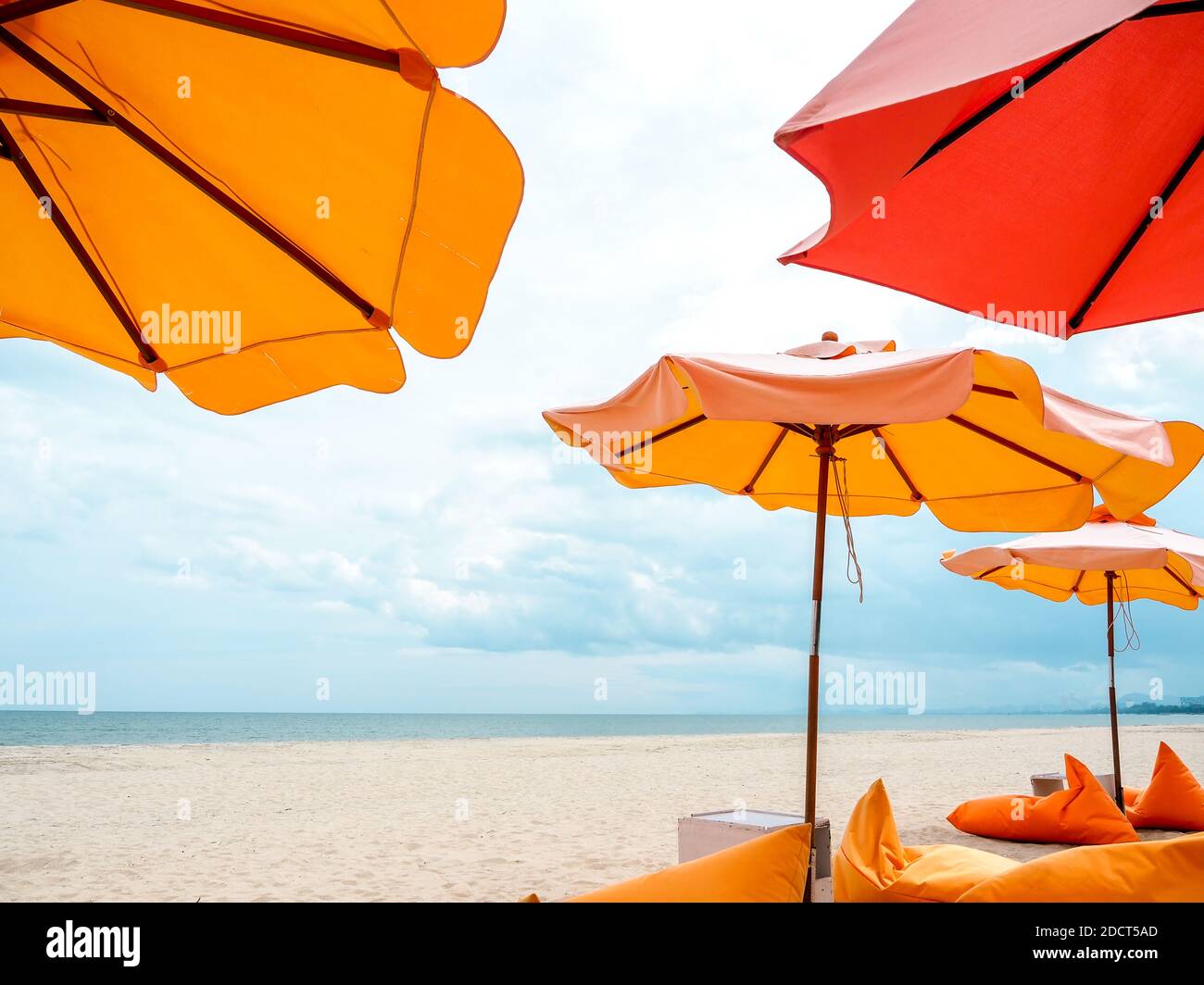 Parasols de plage orange et chaises de sac de haricots sur la plage de sable sur fond bleu ciel avec espace de copie. Banque D'Images