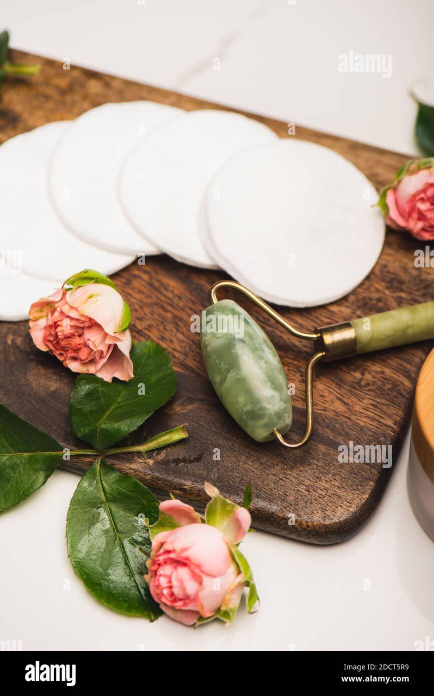 planche à découper avec rouleau de jade, tampons de coton et roses à thé sur fond de marbre blanc Banque D'Images