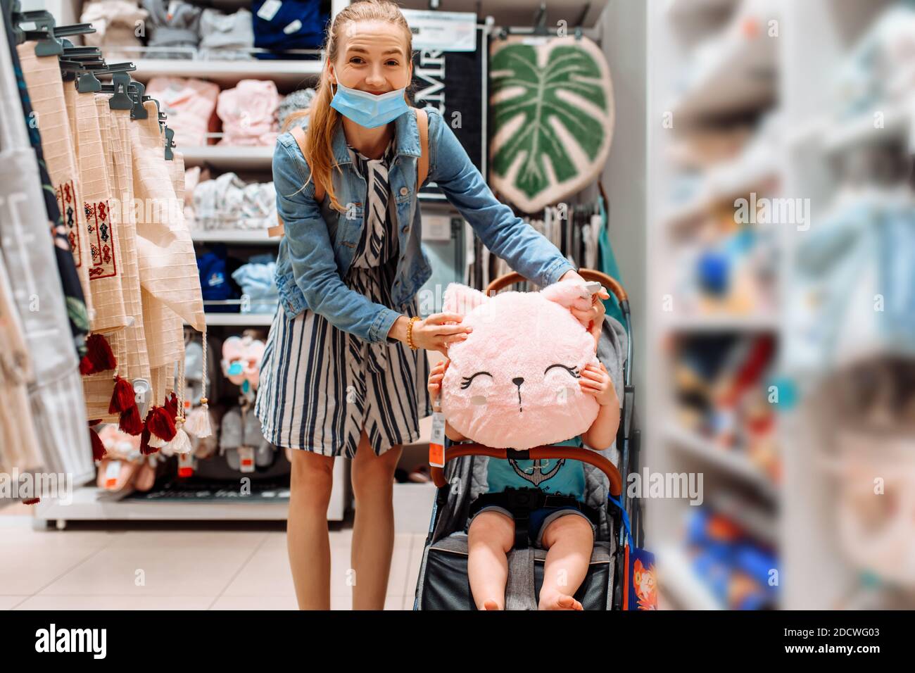 jeune belle femme dans un masque médical protecteur sur son visage, avec un petit enfant dans une poussette, shopping dans un centre commercial. Quarantaine, coronavir Banque D'Images