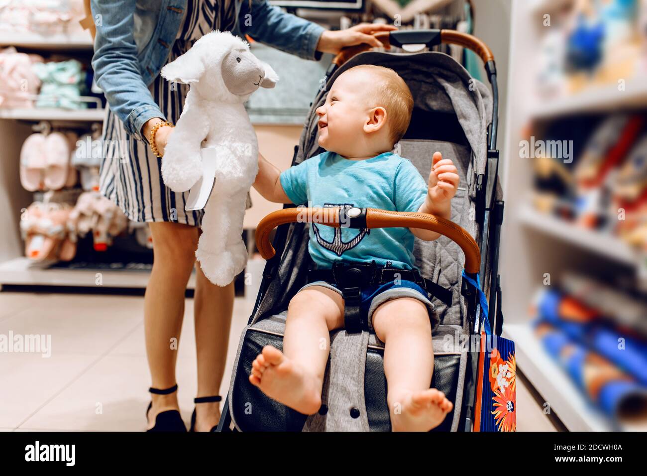 jeune belle femme dans un masque médical protecteur sur son visage, avec un petit enfant dans une poussette, shopping dans un centre commercial. Quarantaine, coronavir Banque D'Images