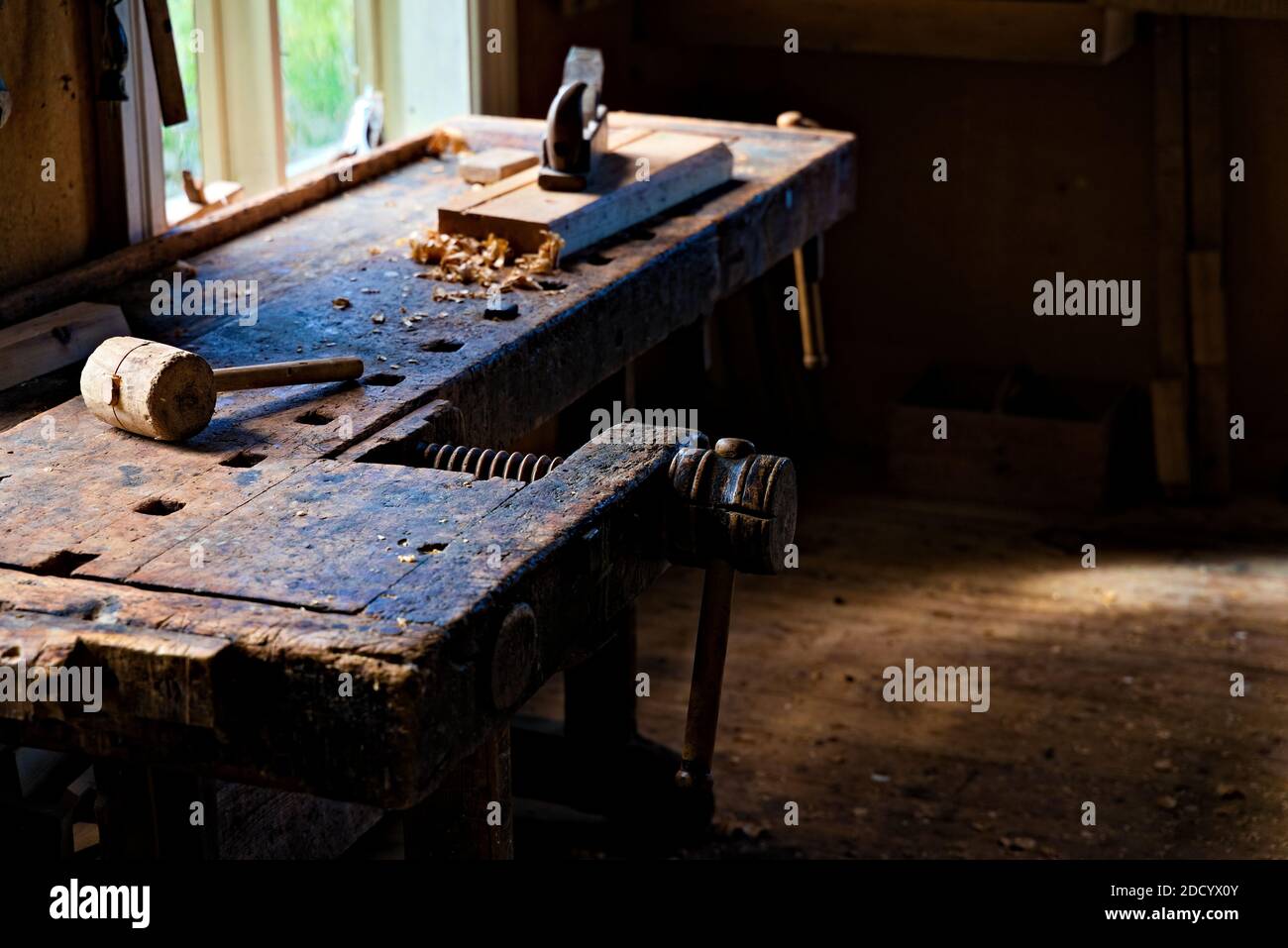 Atelier de menuisiers avec des outils et des sculptures en bois parsemées sur la table et la lumière naturelle qui se diffuse. Banque D'Images