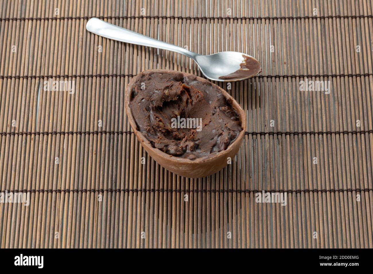 Cuillère en métal avec garniture restante à côté de l'œuf de Pâques. Œuf au chocolat avec garniture au chocolat noir. Banque D'Images