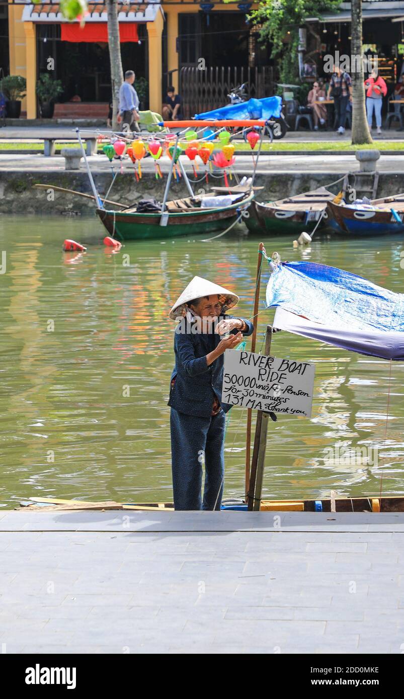 Une vieille femme vietnamienne portant un chapeau conique traditionnel sur un bateau à louer sur le Thu bon River, Hoi an, Vietnam, Asie Banque D'Images