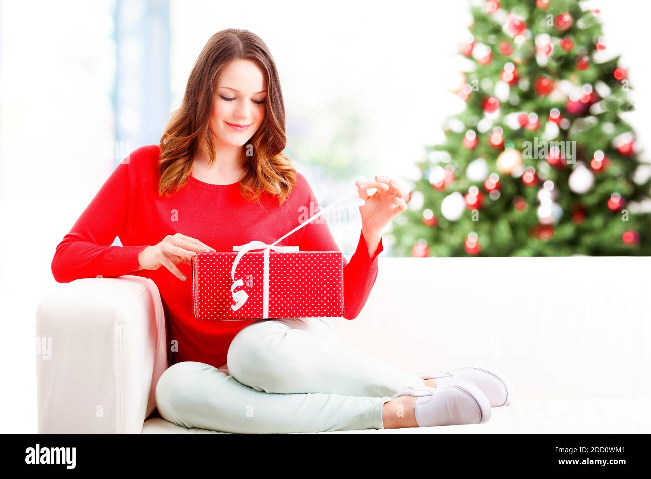 Photo d'une jeune femme heureuse qui déballe son cadeau de noël tout en  étant assise sur le canapé à la maison. L'arrière-plan est arbre de noël  Photo Stock - Alamy