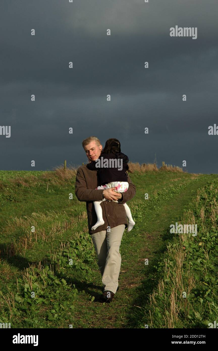 Père transportant une fille de quatre ans loin de la tempête. Octobre. Rundle Hill, South Downs, Goodwood, près de Chichester, West Sussex, Angleterre Banque D'Images