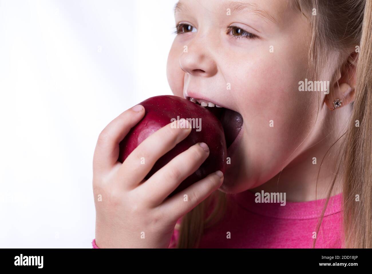 Une petite fille mord une grosse pomme rouge sur fond blanc, gros plan Banque D'Images