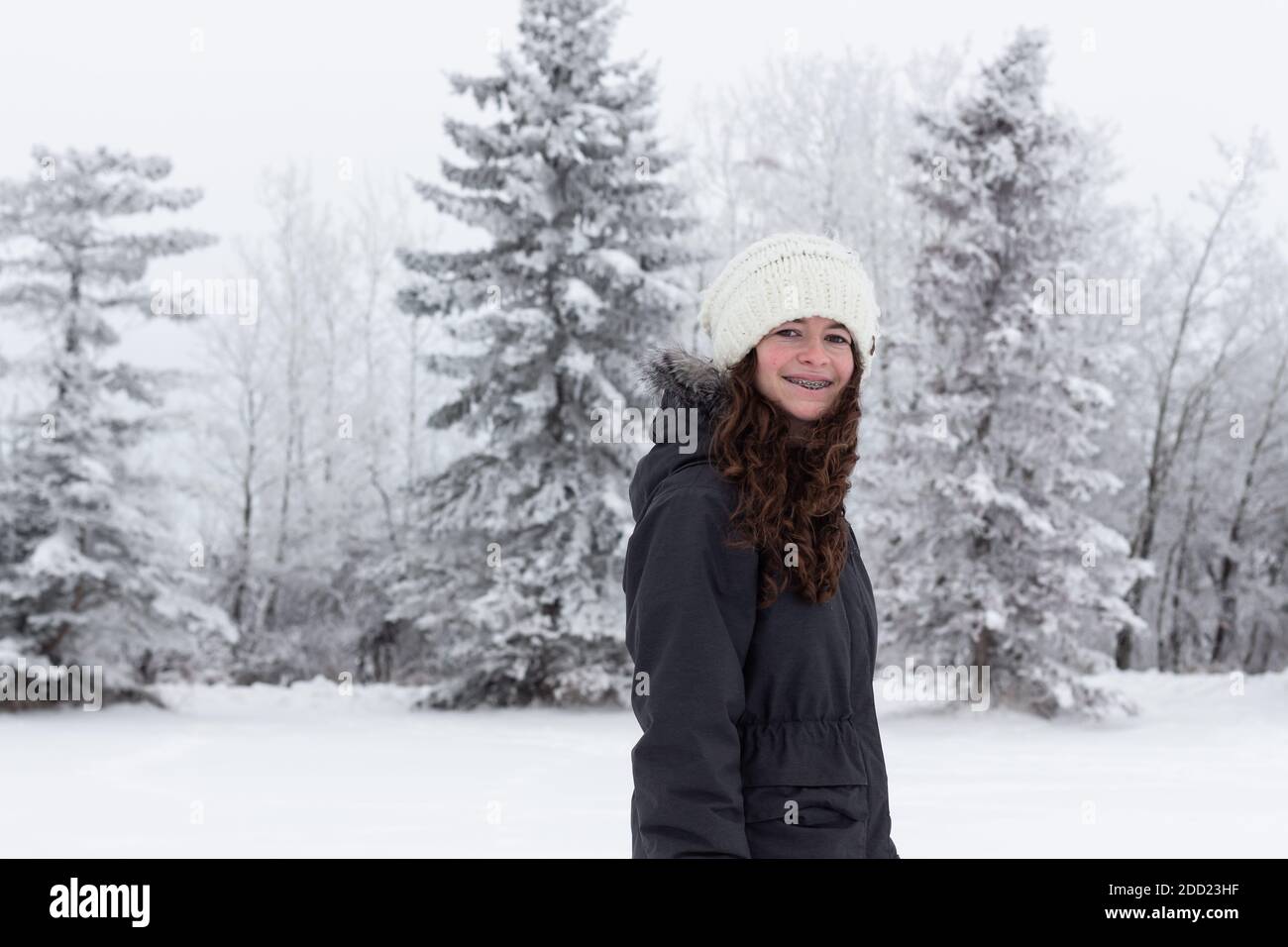 Beau jeune adulte, jeune fille, souriant et marchant dehors en hiver, le gel et la neige sur les arbres et le brouillard dans le ciel MR Images de personnes avec beaucoup de copie Banque D'Images