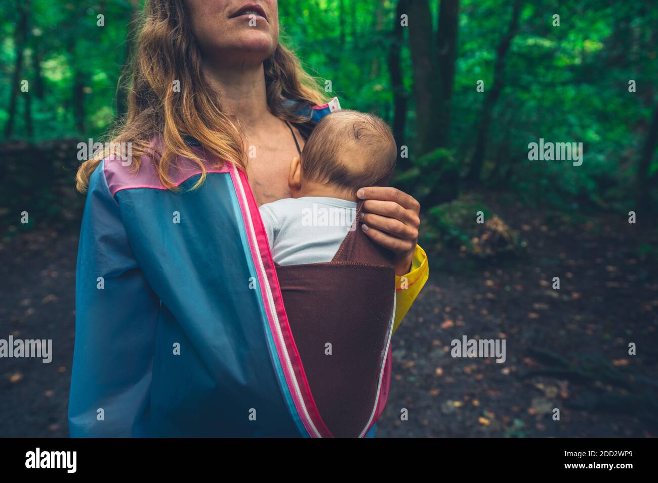 Une jeune mère marche dans la forêt avec elle bébé dans une élingue Banque D'Images