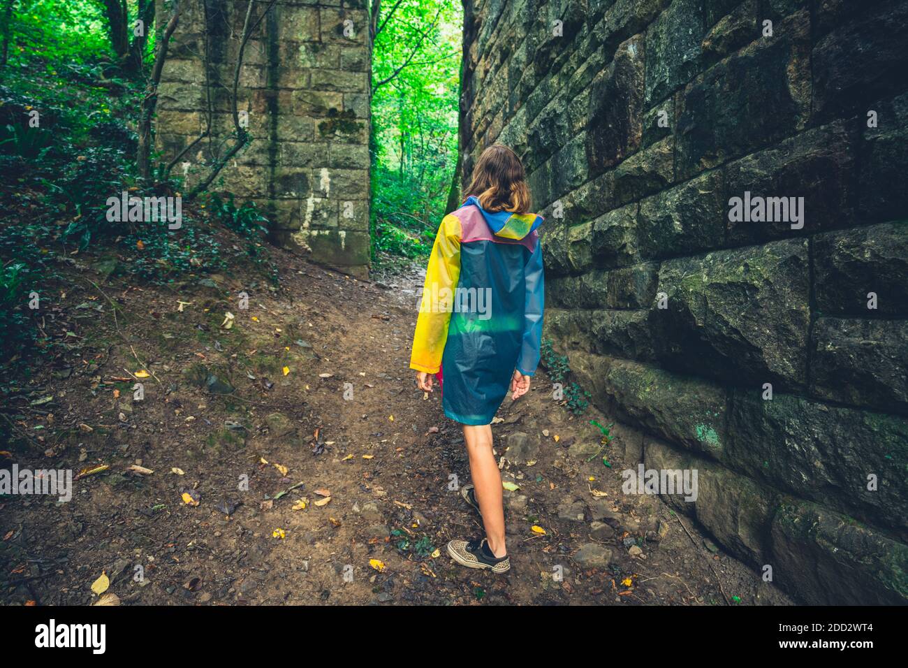 Une jeune femme marche sous une arche de pierre une forêt Banque D'Images
