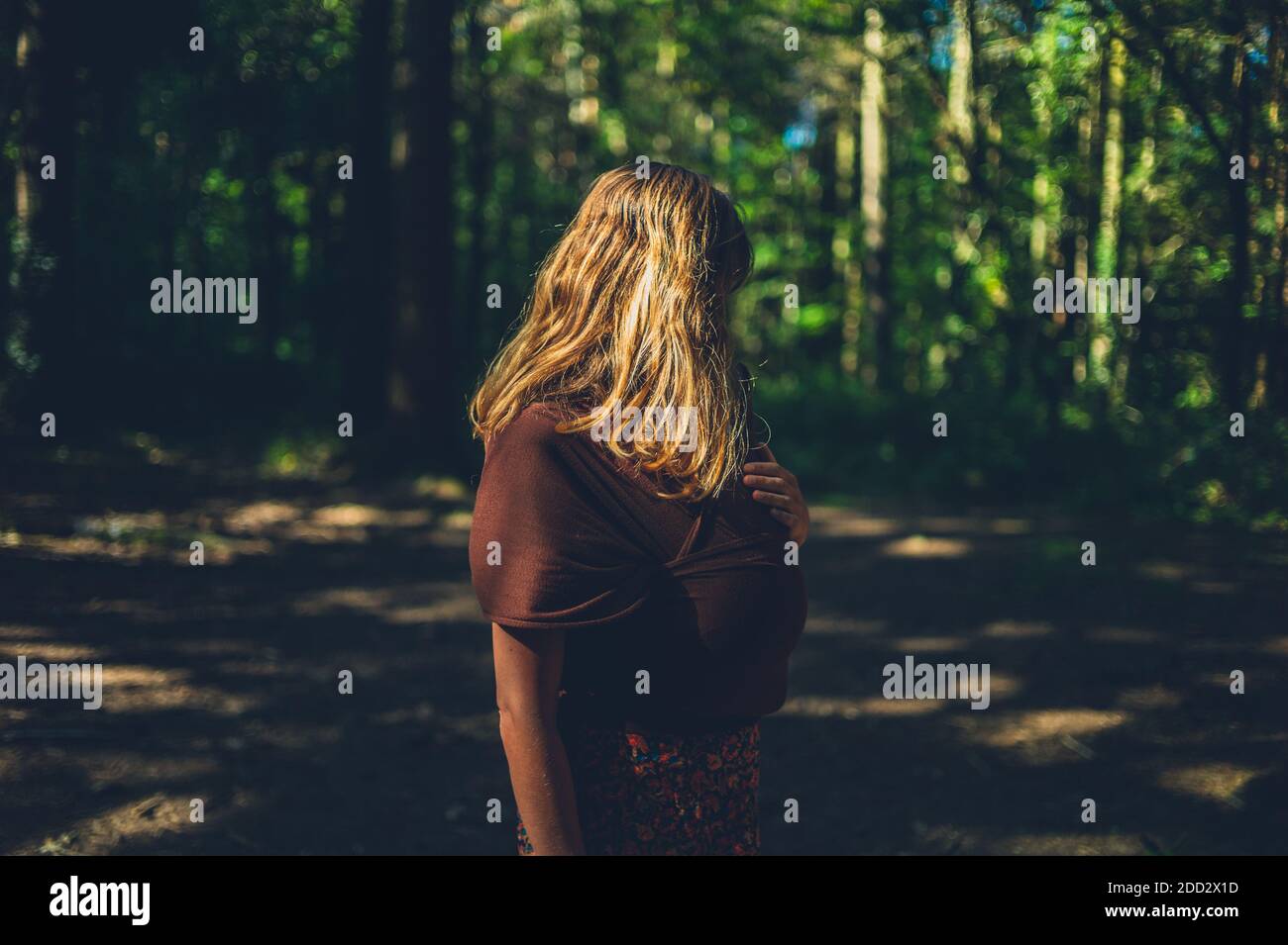 Une jeune mère avec son bébé dans une écharpe est debout dans une forêt Banque D'Images