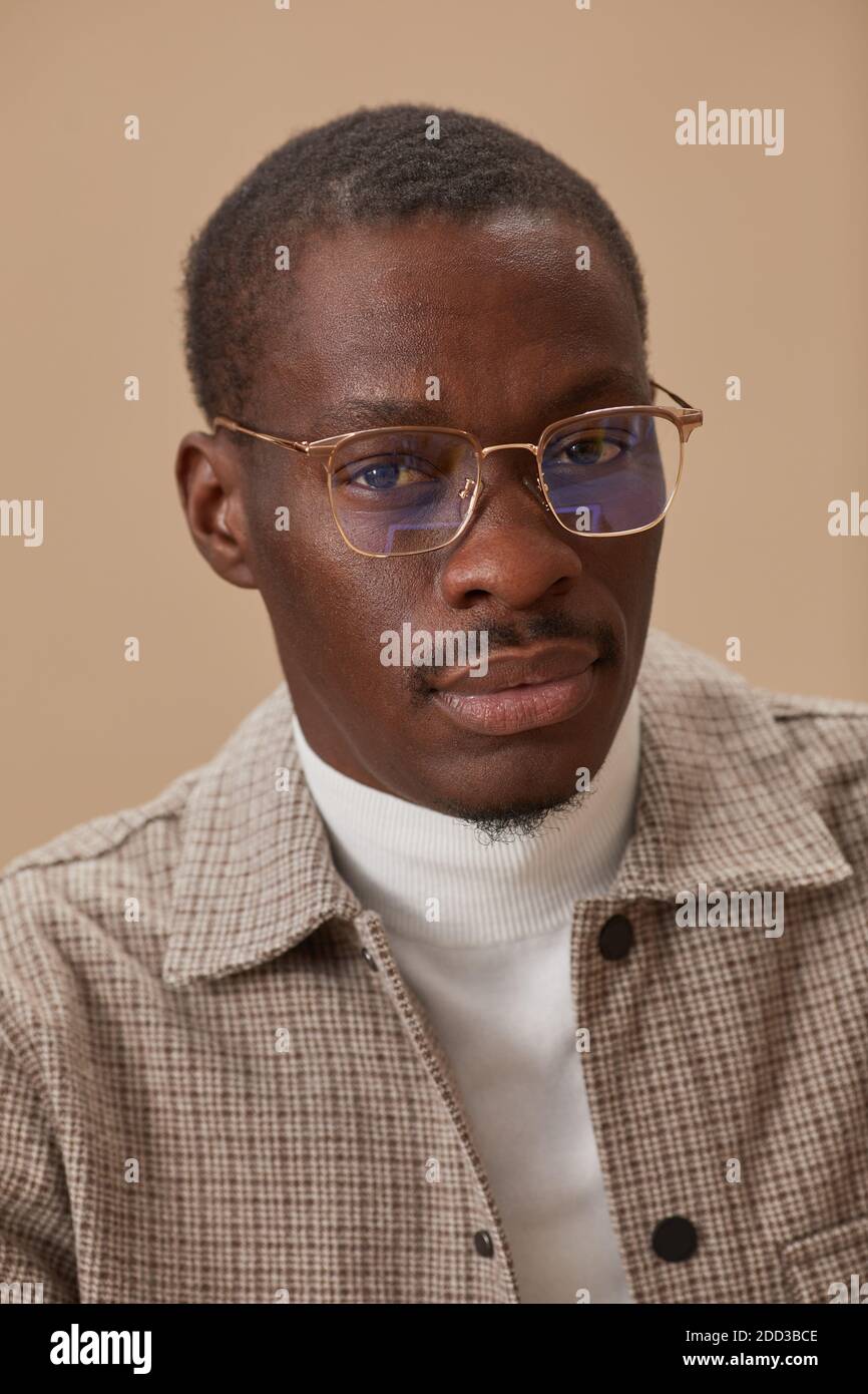 Portrait du jeune homme africain en lunettes et en élégant vêtements regardant l'appareil photo isolés sur fond beige Banque D'Images