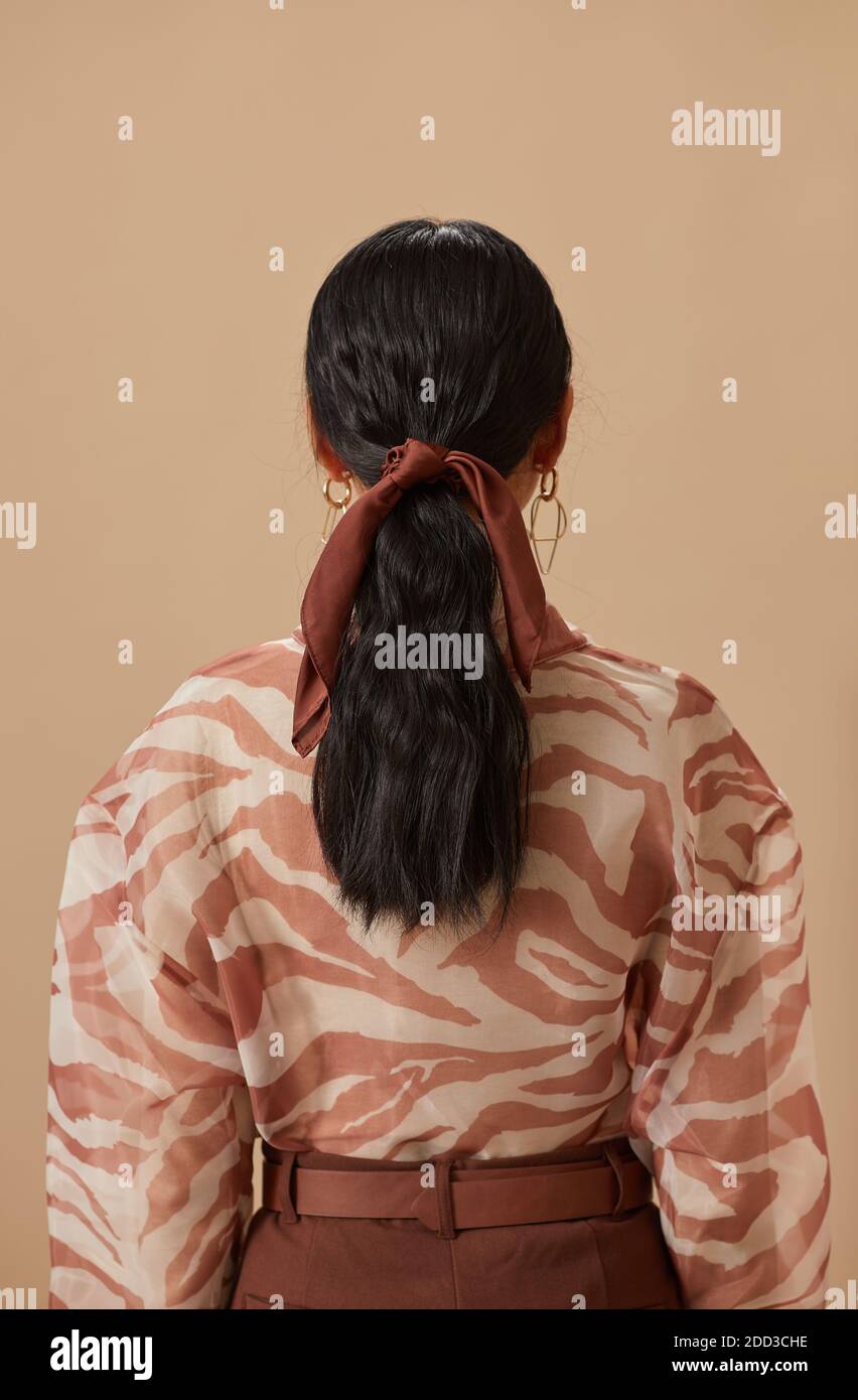Vue arrière de la jeune femme avec les cheveux longs foncés attachés avec ruban sur fond beige Banque D'Images