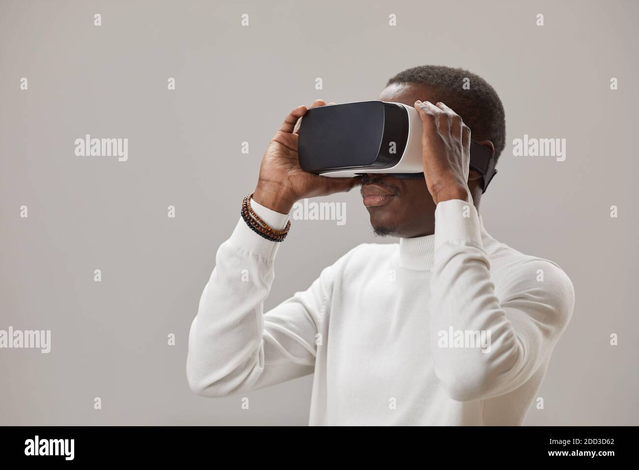 Un jeune homme africain en lunettes virtuelles jouant dans la réalité virtuelle jeu sur fond gris Banque D'Images