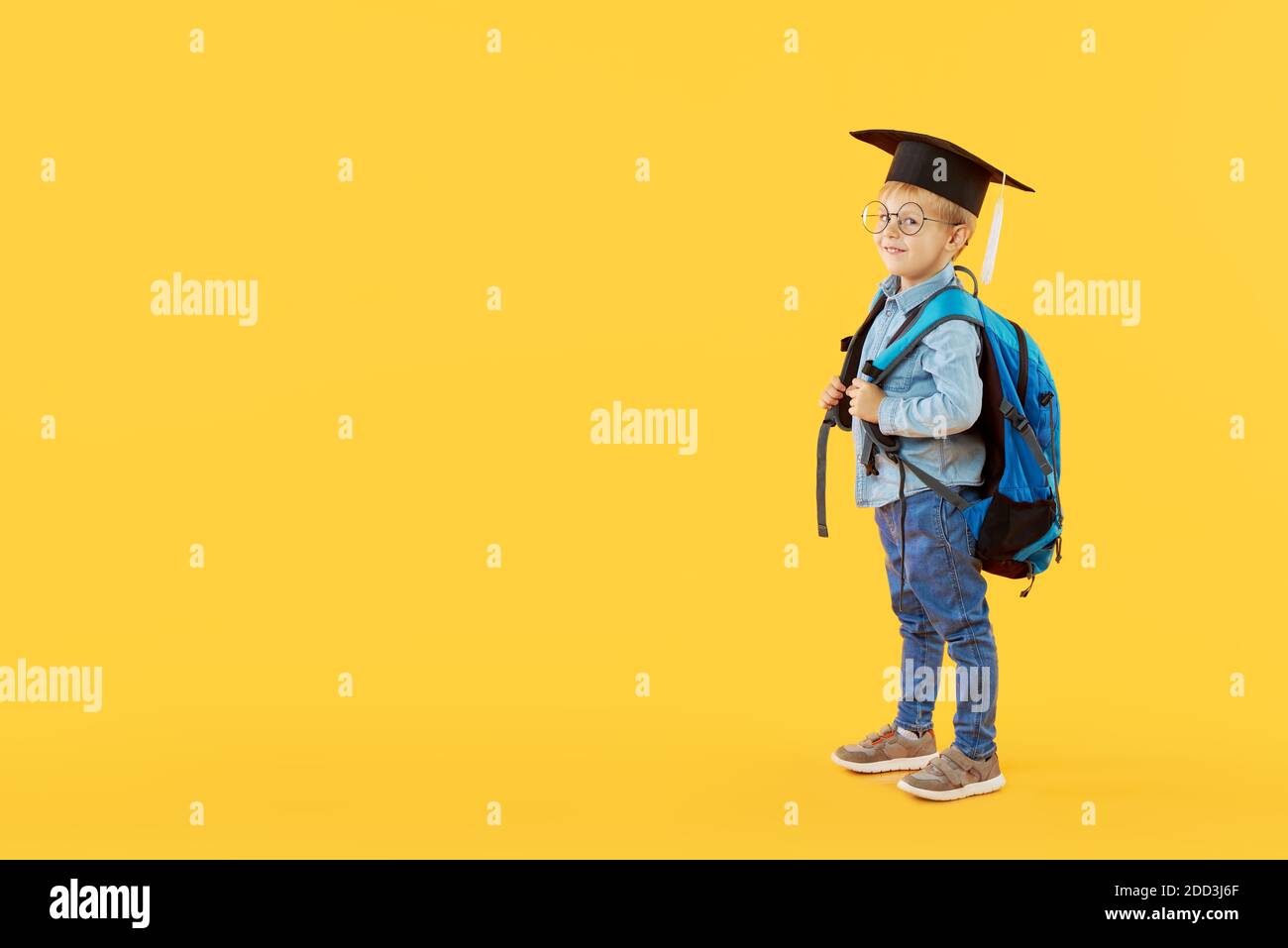 Enfant garçon étudiant à l'école primaire dans une casquette de troisième cycle, des lunettes et avec un sac à dos sur fond jaune. Journée de la connaissance et retour à l'école. Copier l'espace Banque D'Images