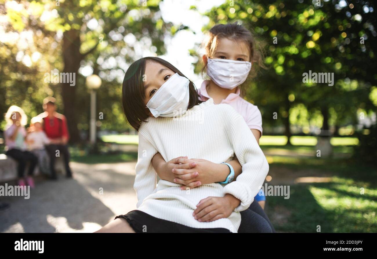 Petites filles d'école avec masque de visage sur terrain de jeu à l'extérieur en ville, coronavirus concept. Banque D'Images