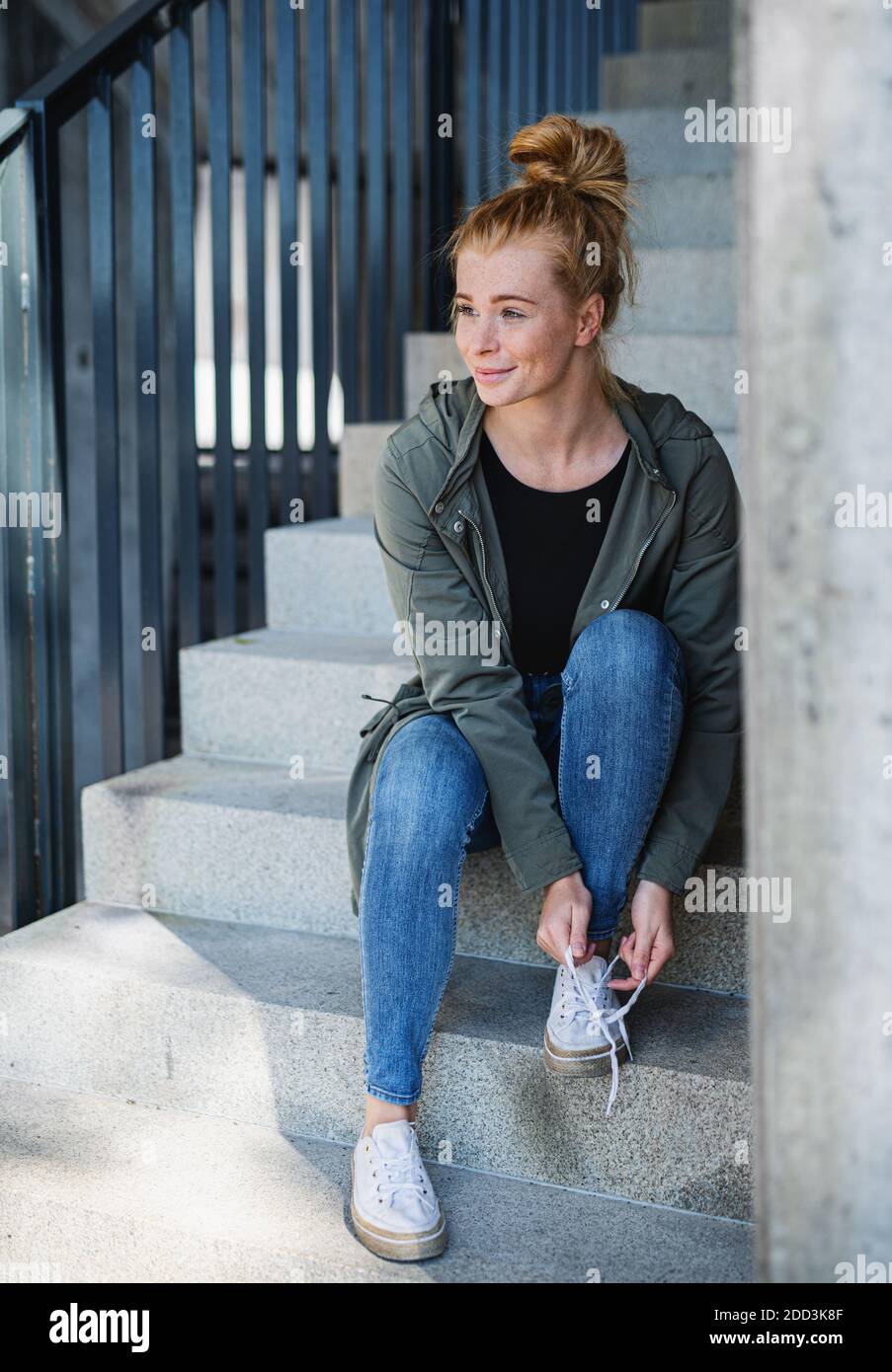 Portrait de jeune femme aux cheveux rouges dehors en ville, nouant des lacets sur l'escalier. Banque D'Images