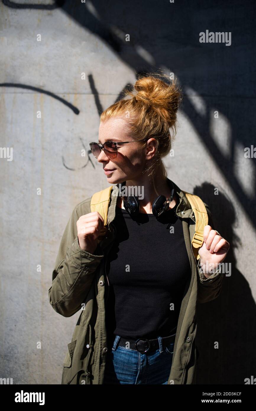 Portrait de la jeune femme heureuse avec des cheveux rouges dehors en ville, portant des lunettes de soleil. Banque D'Images