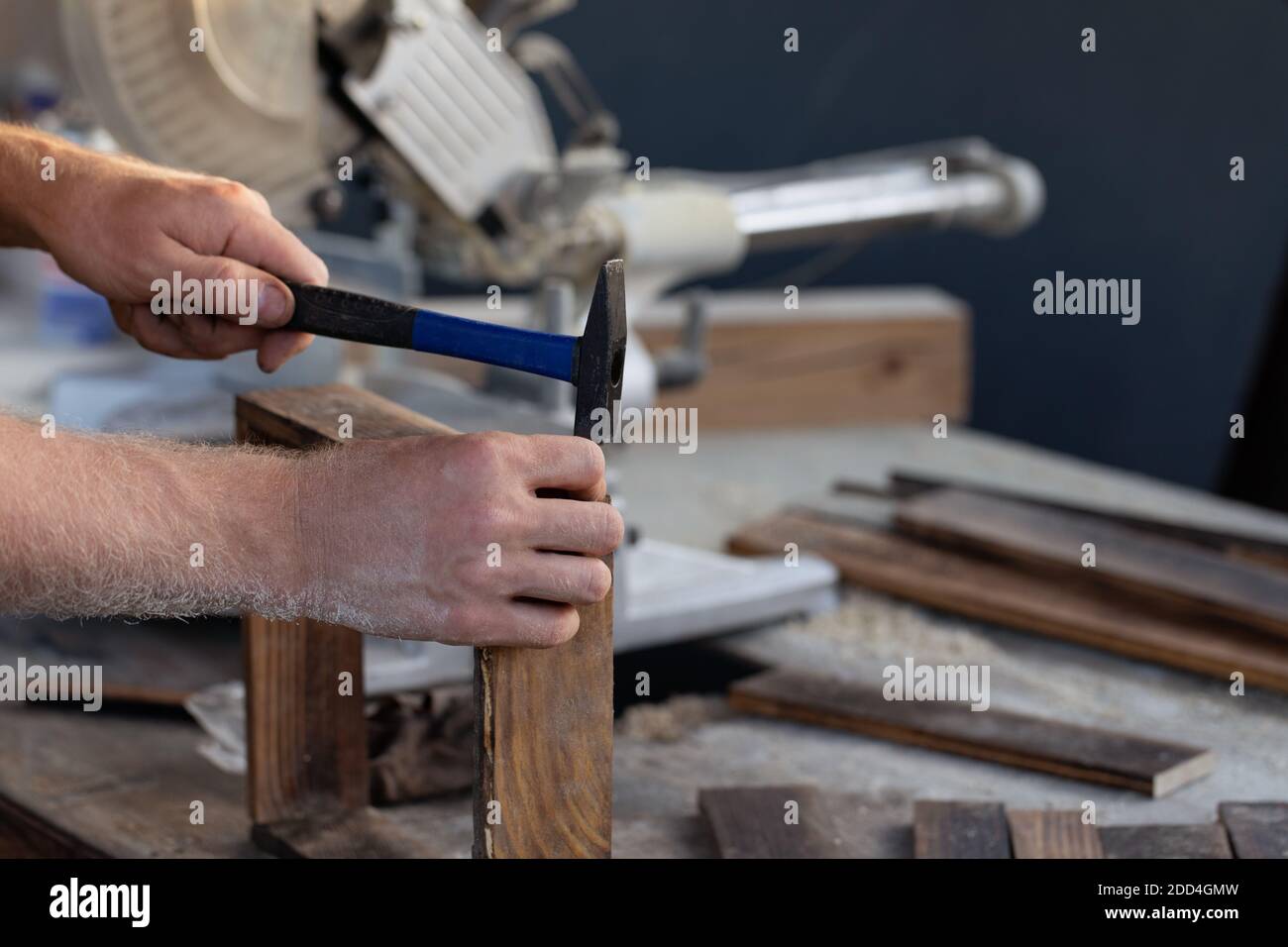 la main de l'homme fait marteler l'ongle sur le bureau en bois dans l'atelier avec arrière-plan de construction Banque D'Images