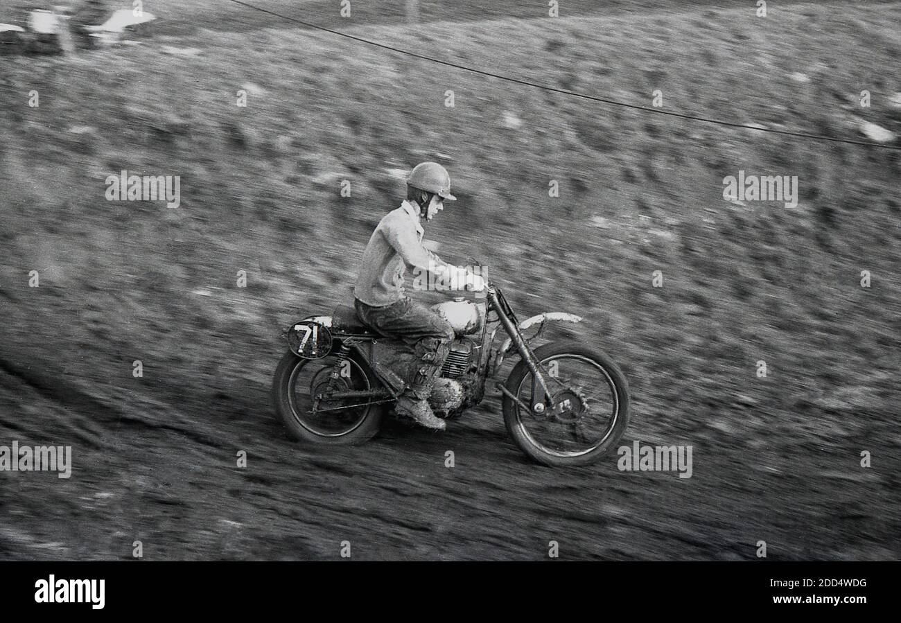 années 1950, historique, moto brouillage...... un concurrent masculin sur une moto participant à une course de brouillage ou de motocycle cross sur un circuit boueux. Camberley dans le Surrey a été le lieu de la première course de Scramble en 1924. Au cours des années suivantes, le sport gagne en popularité, en particulier en Grande-Bretagne où des équipes des constructeurs de motos britanniques classiques, dont la Birmingham Small Arms Company (BSA), Norton, Matchless, Rudge et AJS participent à des courses. Banque D'Images