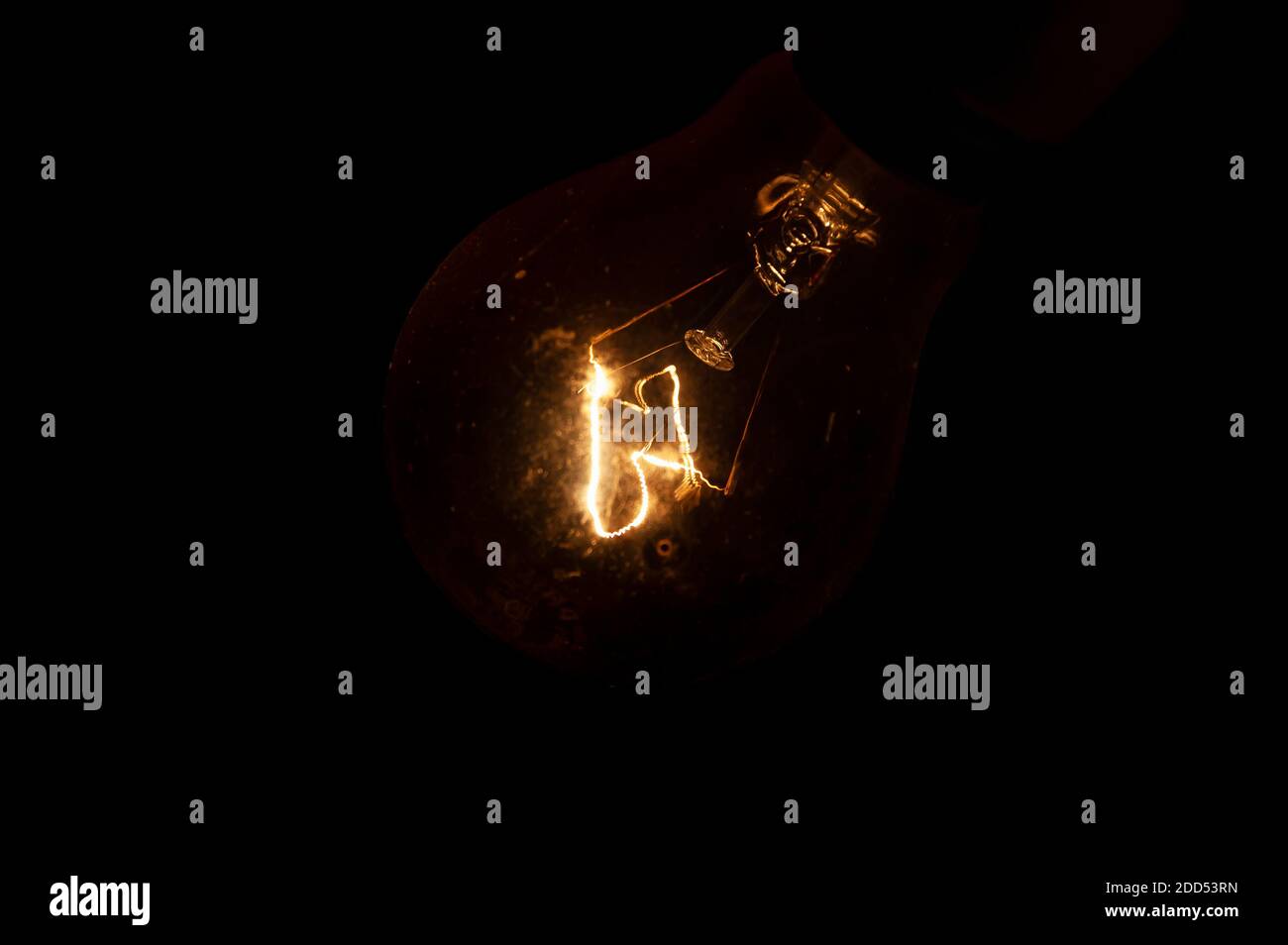 Filament en fil de tungstène incandescent d'une ampoule à incandescence, produisant de la lumière, isolée sur un fond noir. Banque D'Images