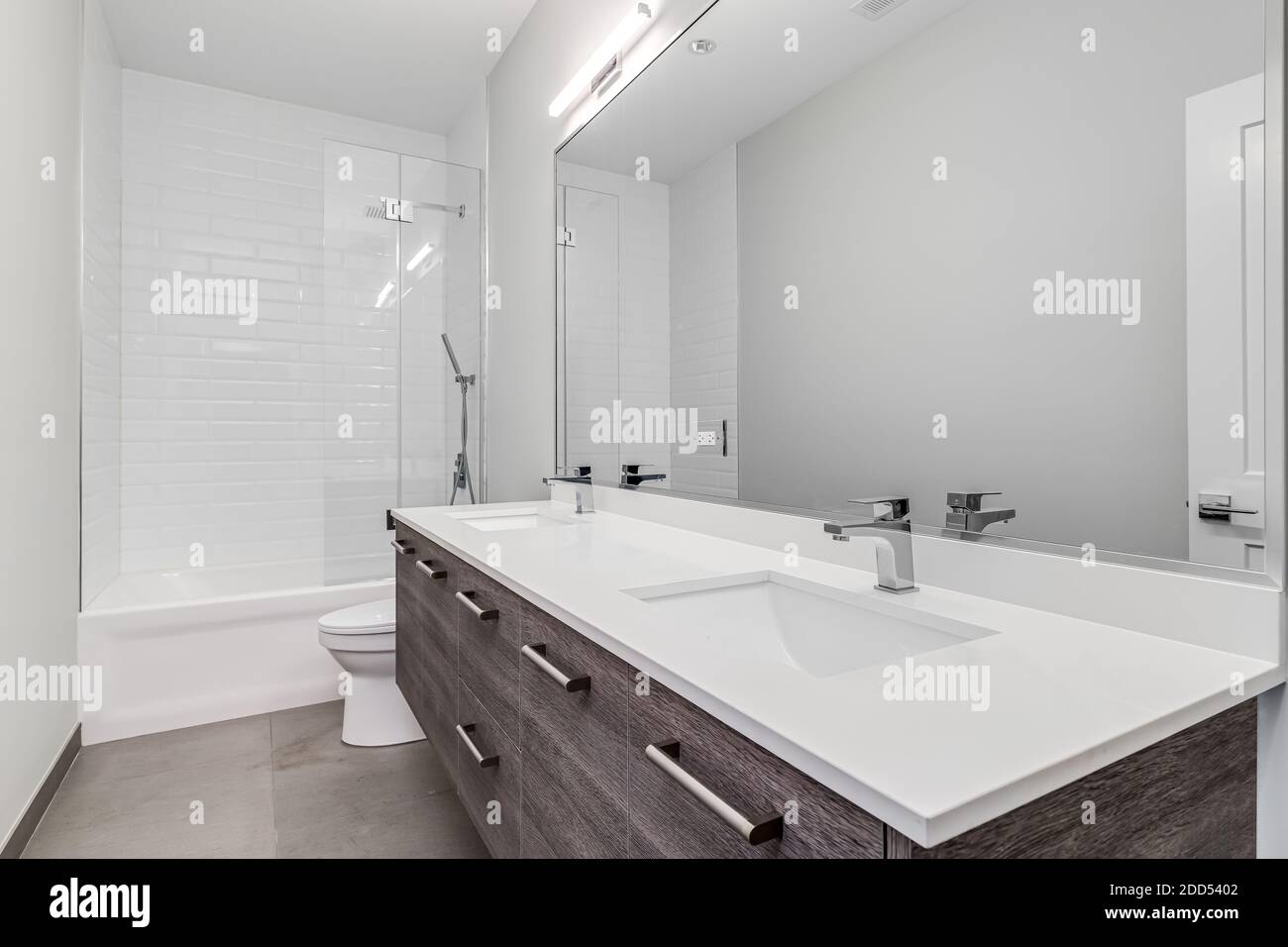 Salle de bains de luxe avec meuble-lavabo en bois, comptoir blanc et robinets chromés avec douche carrelée de blanc. Banque D'Images