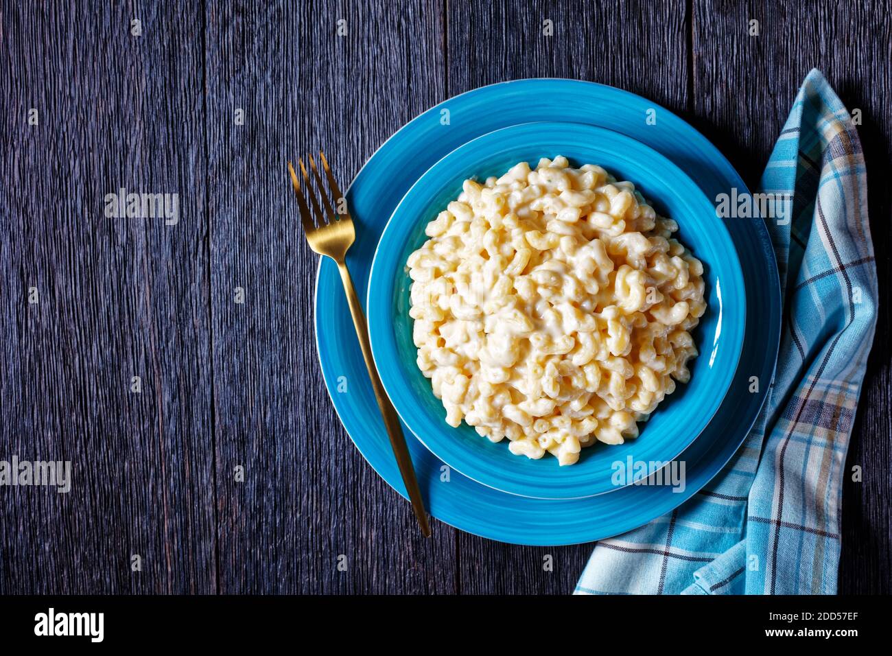 mac classique et fromage dans un bol bleu avec fourchette dorée et serviette sur une table en bois, vue horizontale depuis le dessus, plat, espace libre Banque D'Images