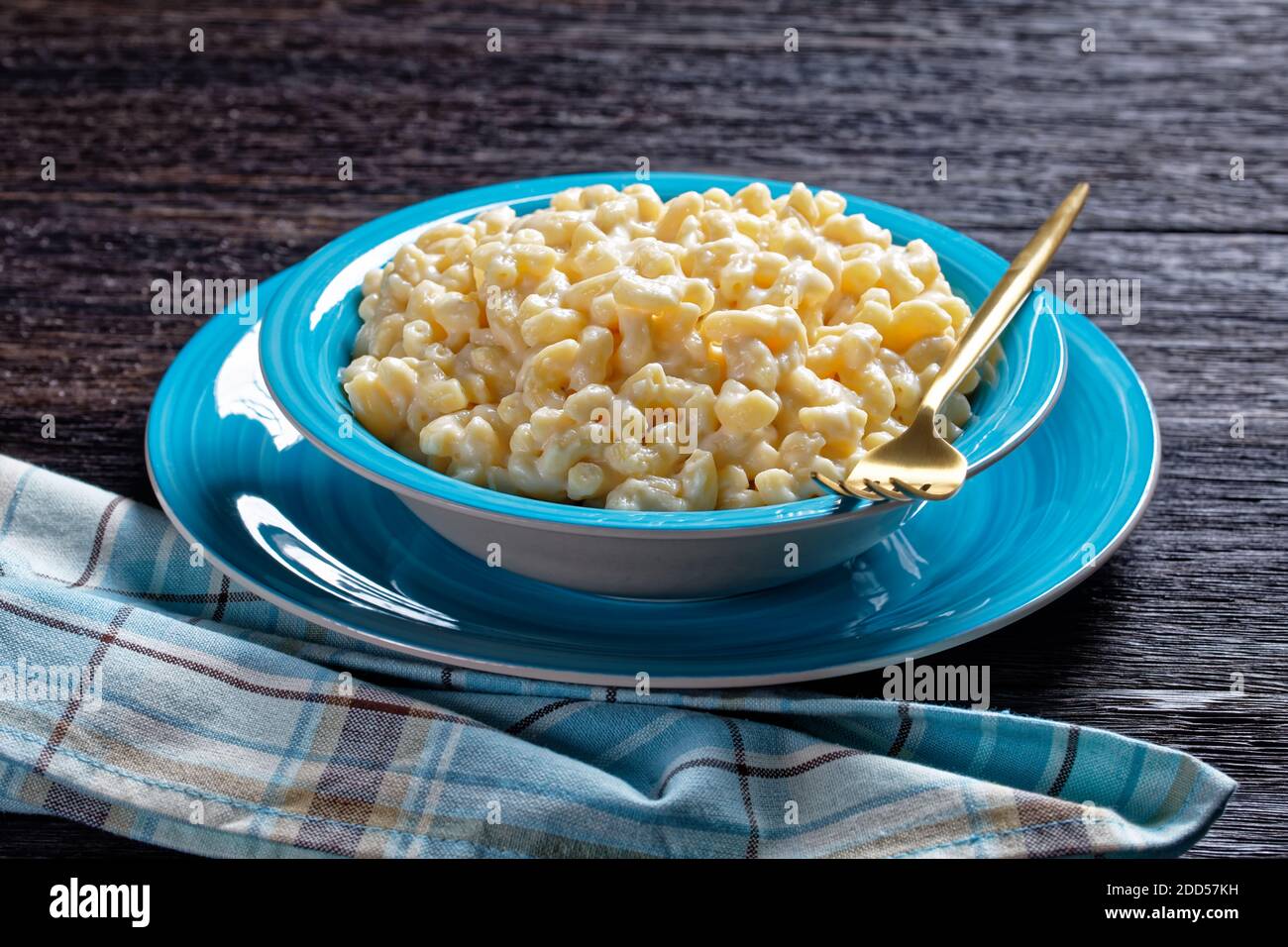 mac et fromage dans un bol bleu avec fourchette dorée et serviette sur une table en bois, vue horizontale depuis le dessus Banque D'Images