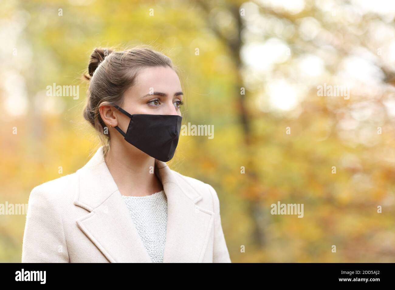 Femme sérieuse avec masque marchant dans un parc en hiver vue sur l'extérieur Banque D'Images