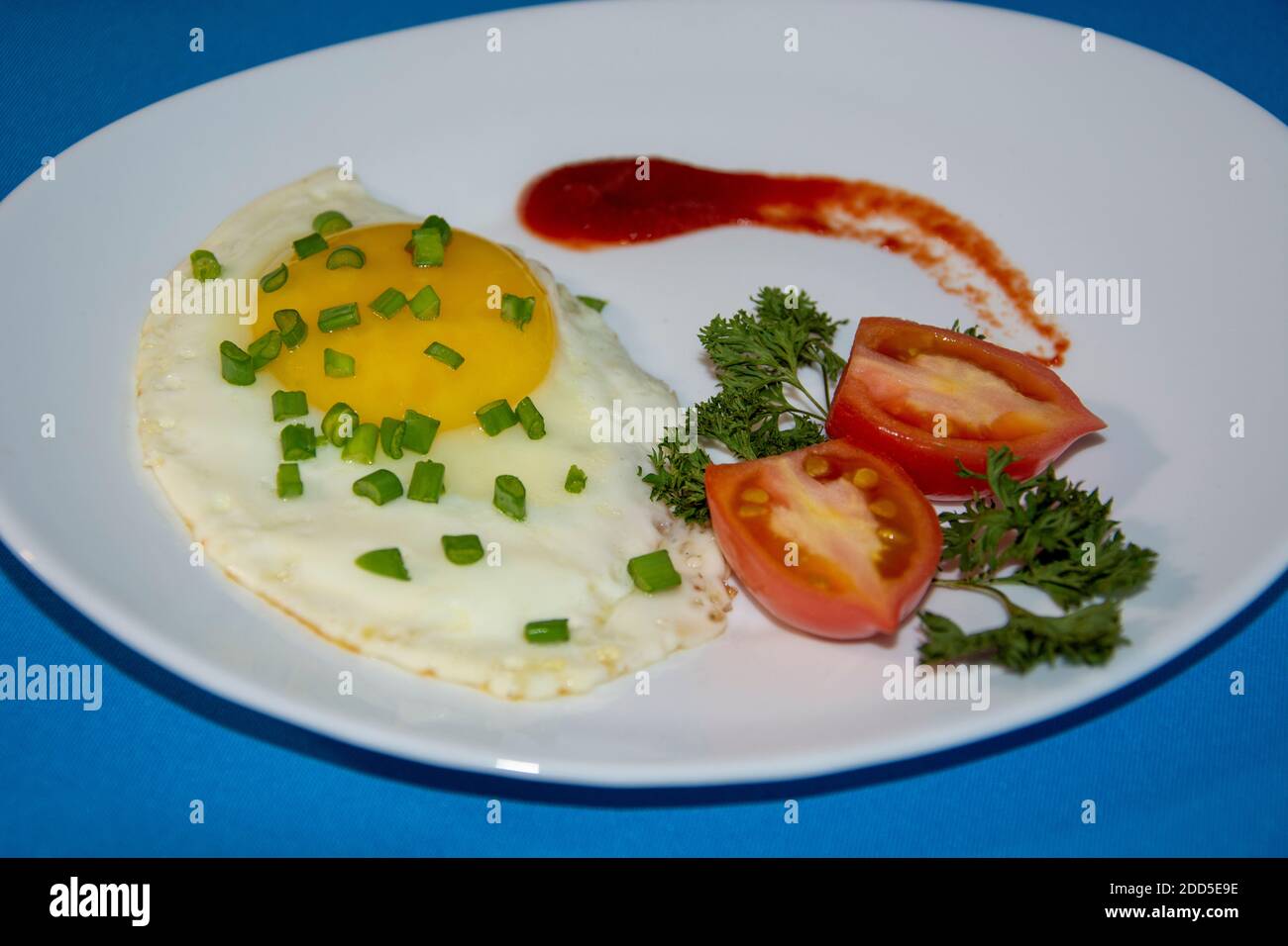 Un plat d'œufs frits. Œufs frits sur une assiette blanche avec tomates, herbes, ketchup. Petit déjeuner de baccalauréat. Banque D'Images