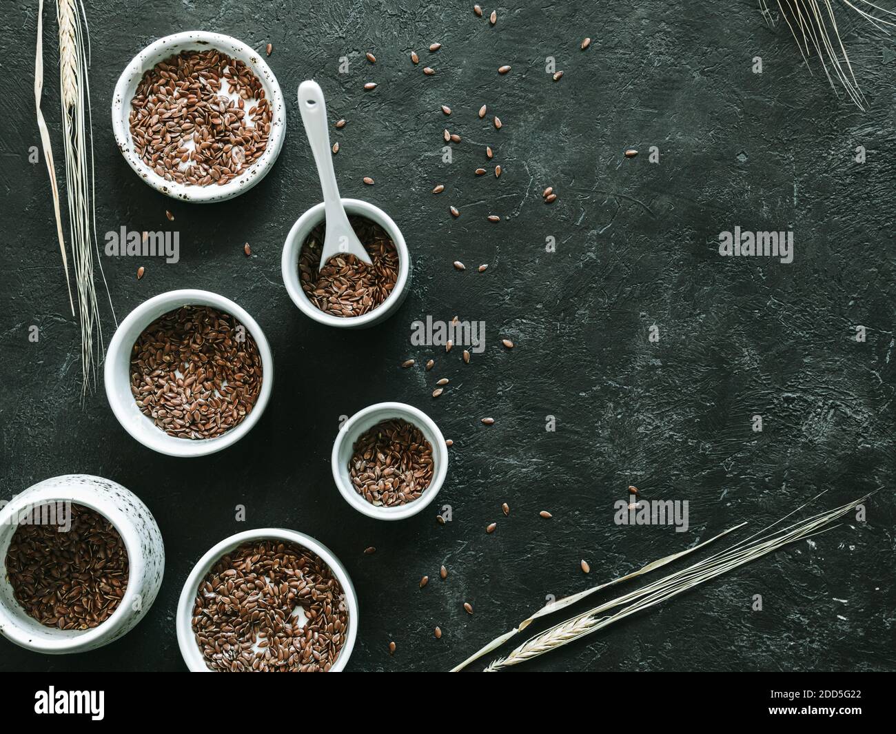 graines de lin et oreille de seigle sèche sur fond sombre. Ensemble de petits bols avec graines de lin biologique ou graines de lin. Les graines de lin sont riches en acides gras oméga-3. Copier l'espace. Vue de dessus ou à plat. Banque D'Images