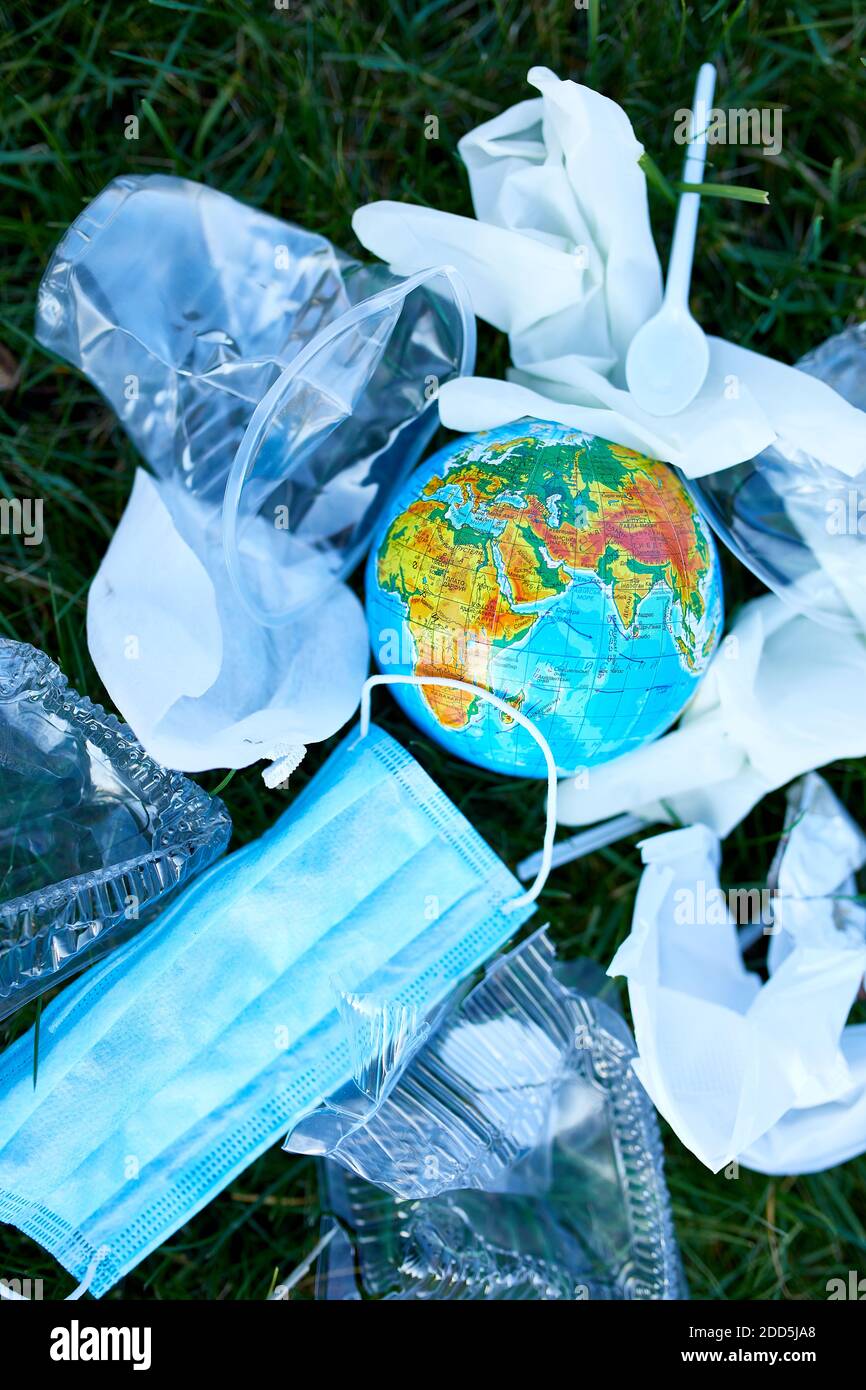 Un globe dans une pile de déchets éparpillés sur un fond d'herbe verte, autour de plastique dispersé, masque de protection, gants, déchets pendant la casserole du coronavirus Banque D'Images