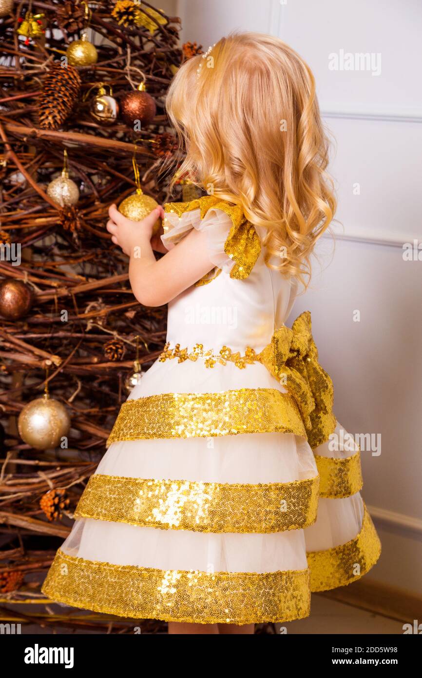 Une petite fille dans une robe blanche et or chic se tient avec son dos à  l'appareil photo et décorent l'arbre de Noël Photo Stock - Alamy