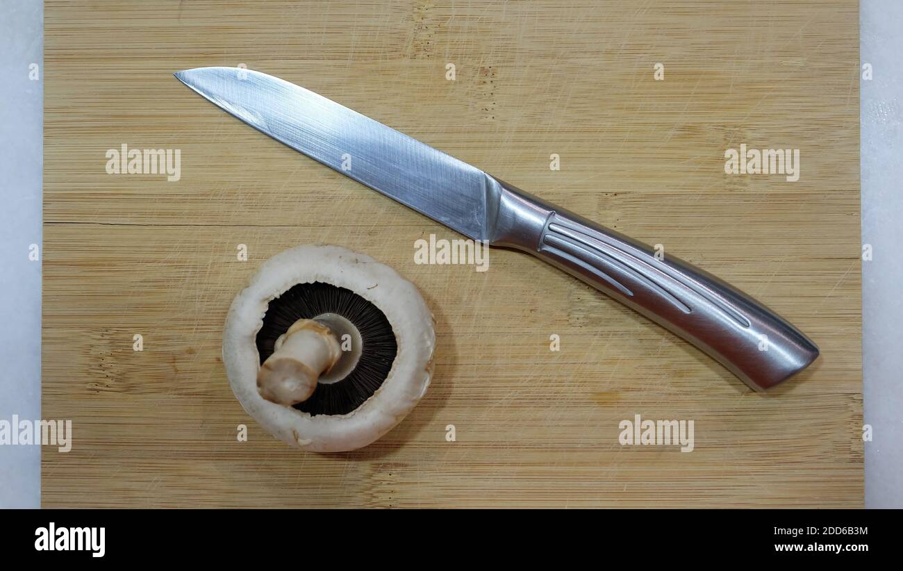 Un seul champignon blanc sur une planche à découper en bois, avec un couteau de forme à côté. Banque D'Images