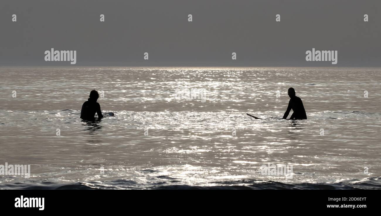 deux surfeurs attendent dans la lumière du soir pour la vague parfaite, profitant de la paix et de la tranquillité du moment Banque D'Images