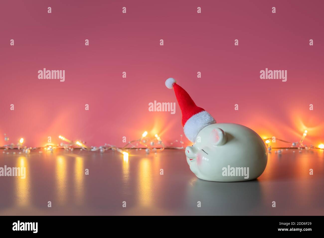 Tirelire dans le chapeau du Père Noël et guirlande brillante sur fond rose. Concept d'économies pour Noël et nouvel an, vacances. Copier l'espace pour te Banque D'Images