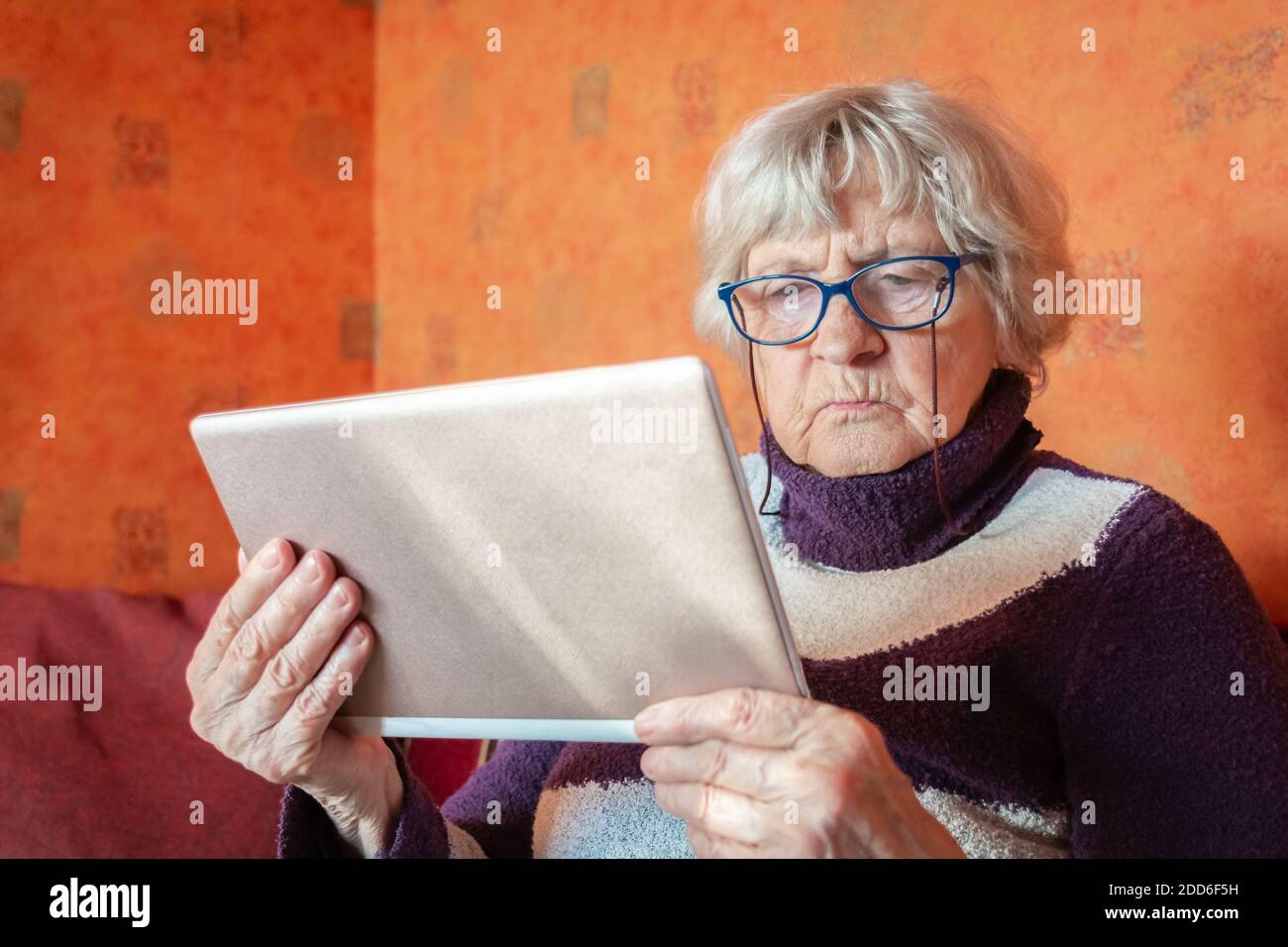 Femme âgée en lunettes utilisant une tablette et assise sur un canapé à la maison. Grand-mère tenant un appareil numérique entre les mains. Cheveux gris vieille dame regardant la table Banque D'Images