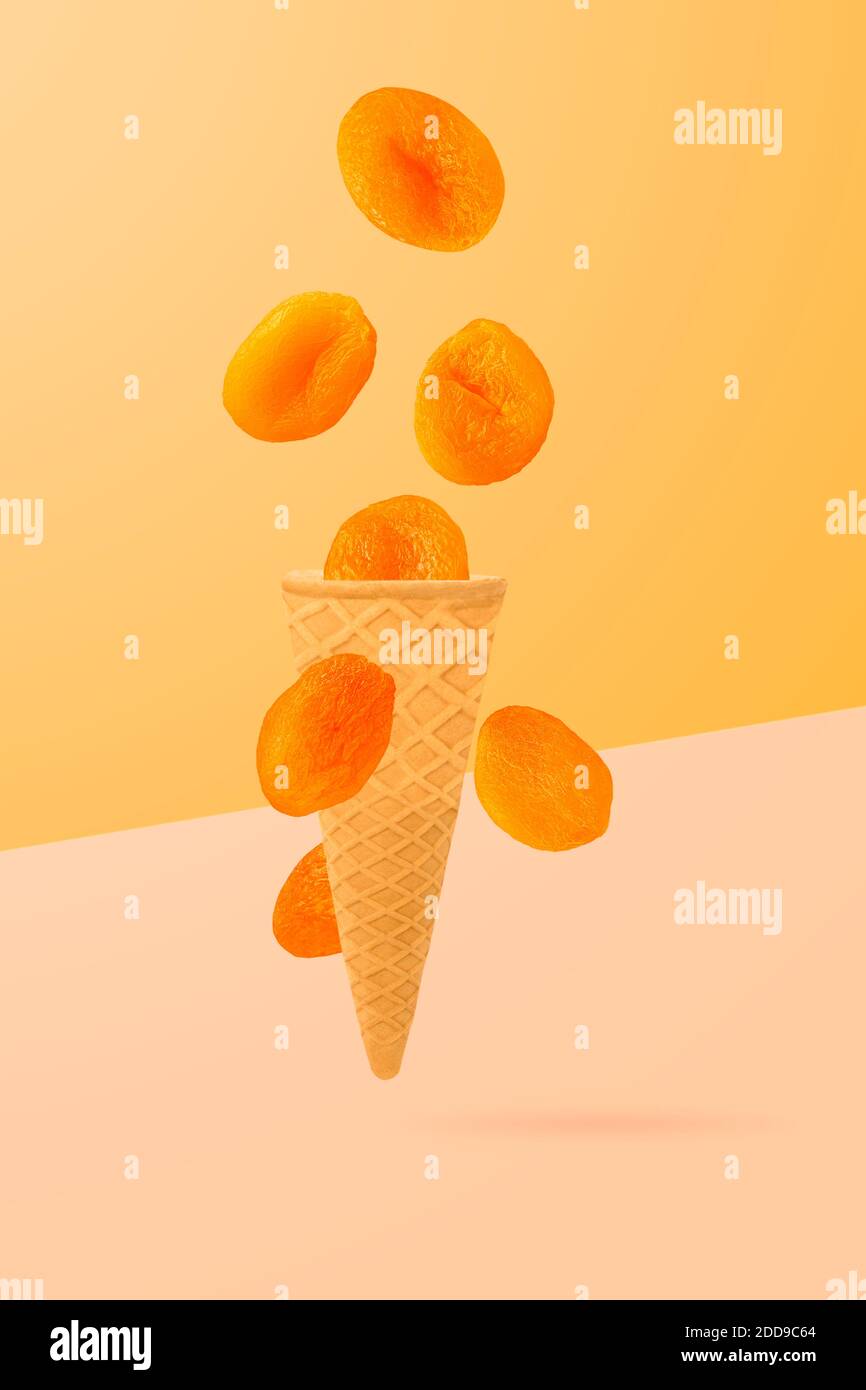 Cône de glace isolé avec des fruits dans l'air. Abricots séchés tombant isolés sur fond jaune avec passe-cheveux comme élément de conception d'emballage et Banque D'Images