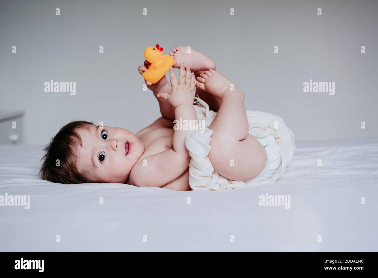 Bébé garçon mignon jouant avec un jouet de canard tout en étant allongé sur le lit à la maison Banque D'Images