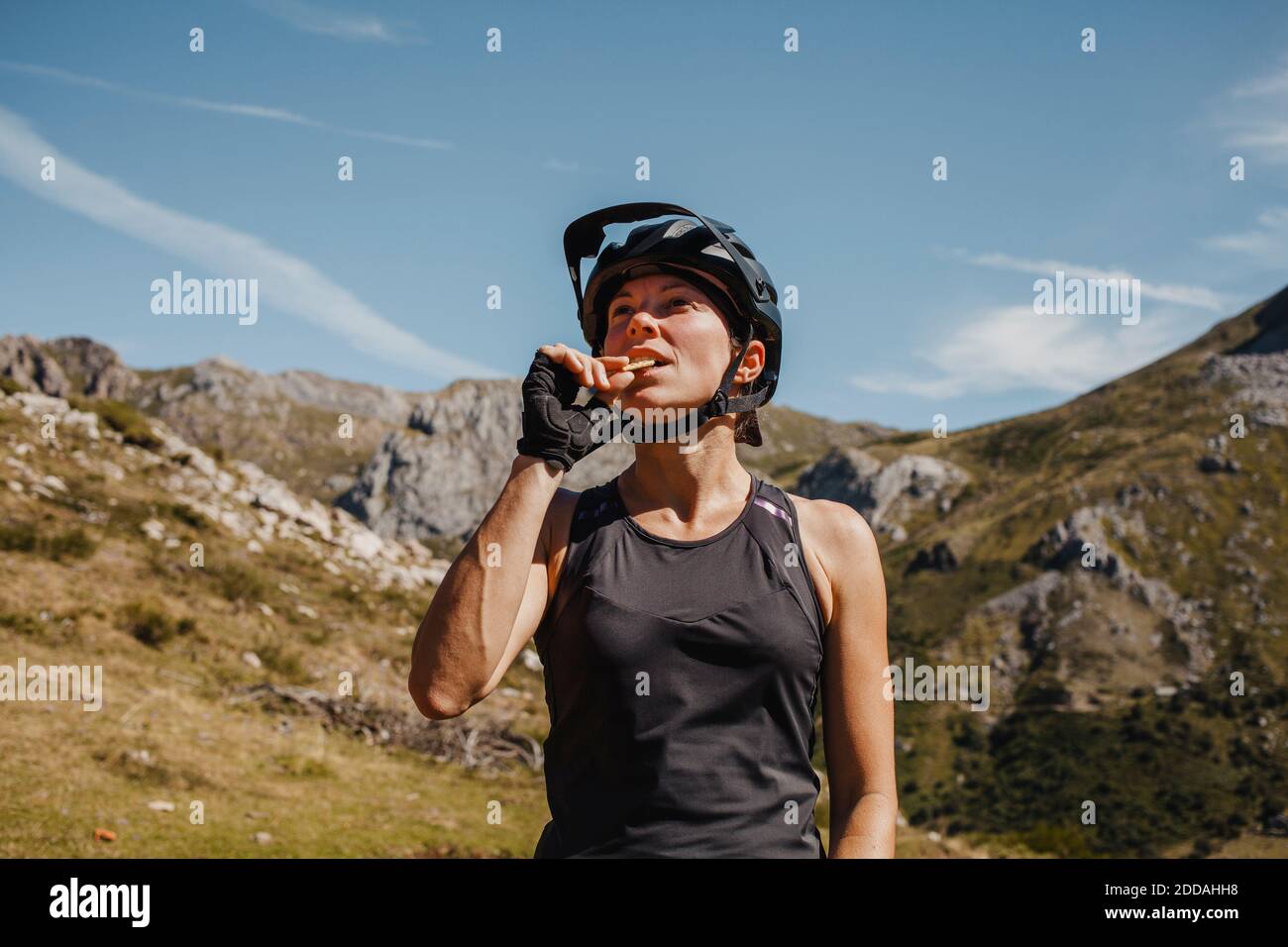 Femme portant un casque de vélo mangeant biscuit tout en se tenant contre la montagne au parc naturel de Somiedo, Espagne Banque D'Images