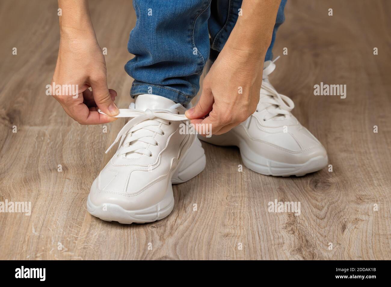 Les mains de femme caucasienne nouent des lacets élastiques sur la grosse  semelle des sneakers blanches sur ses pieds sur le sol brun. Nouvelles  chaussures confortables pour un style de vie actif
