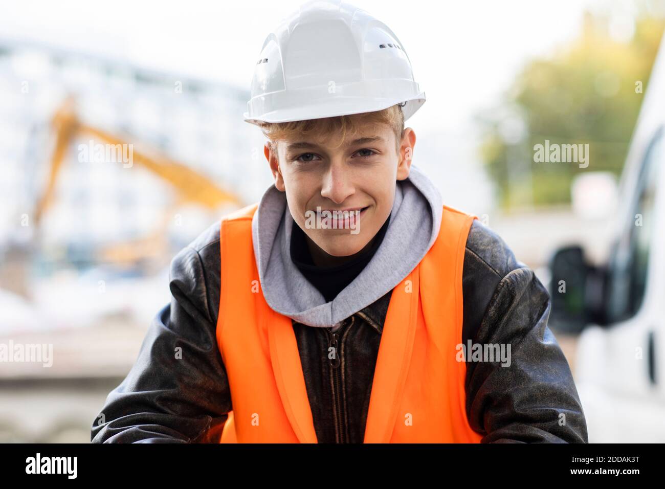 Adolescent souriant stagiaire en construction portant un casque et des vêtements réfléchissants à site Banque D'Images