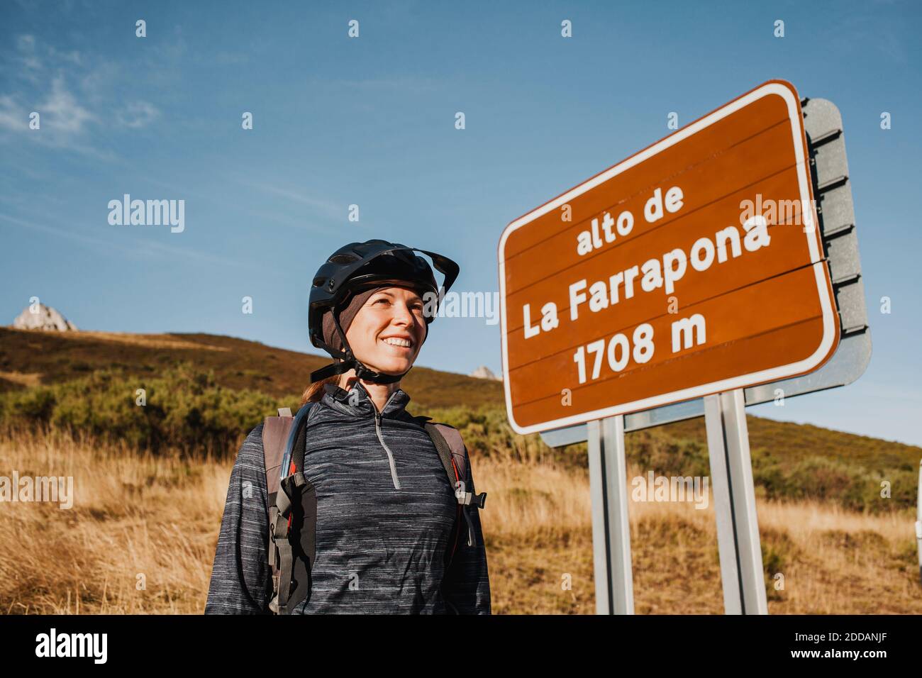 Femme mi-adulte souriante portant un casque de cyclisme debout près du panneau au parc naturel de Somiedo, Espagne Banque D'Images