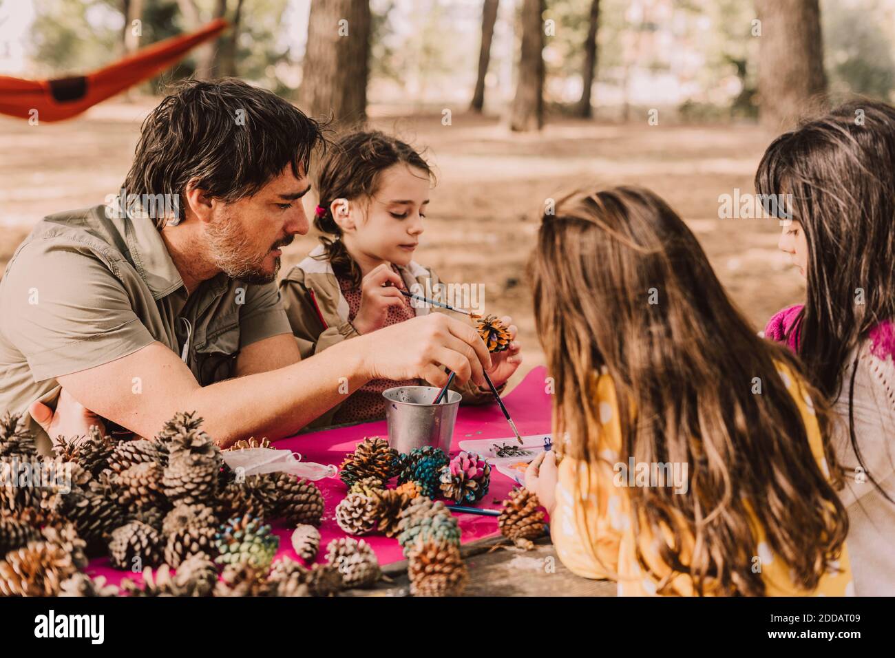 Homme mature avec des filles décorant tout en colorant des cônes de pin à table de pique-nique dans le parc Banque D'Images
