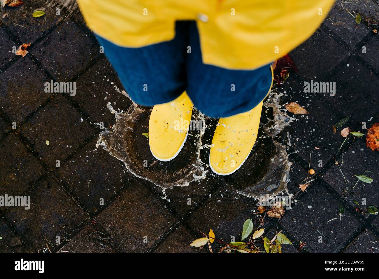 Femme portant des bottes jaunes sautant sur la flaque pendant la saison des pluies Banque D'Images